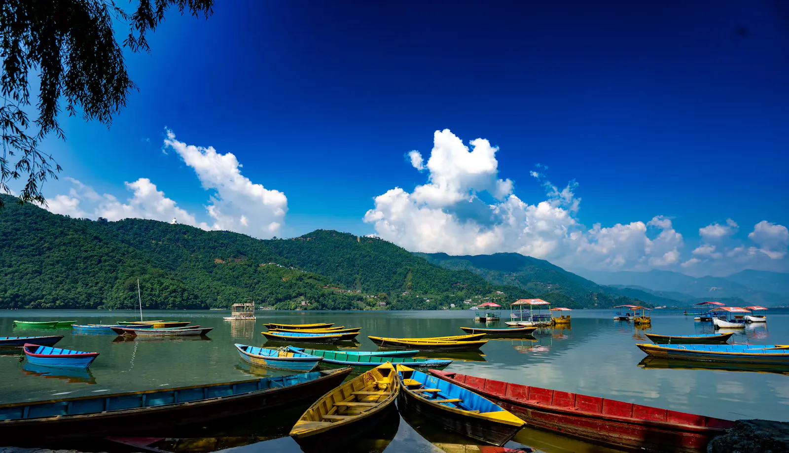 Colourful wooden rowing boats on Phewa Lake in Pokhara, Nepal, with green hills and white clouds behind