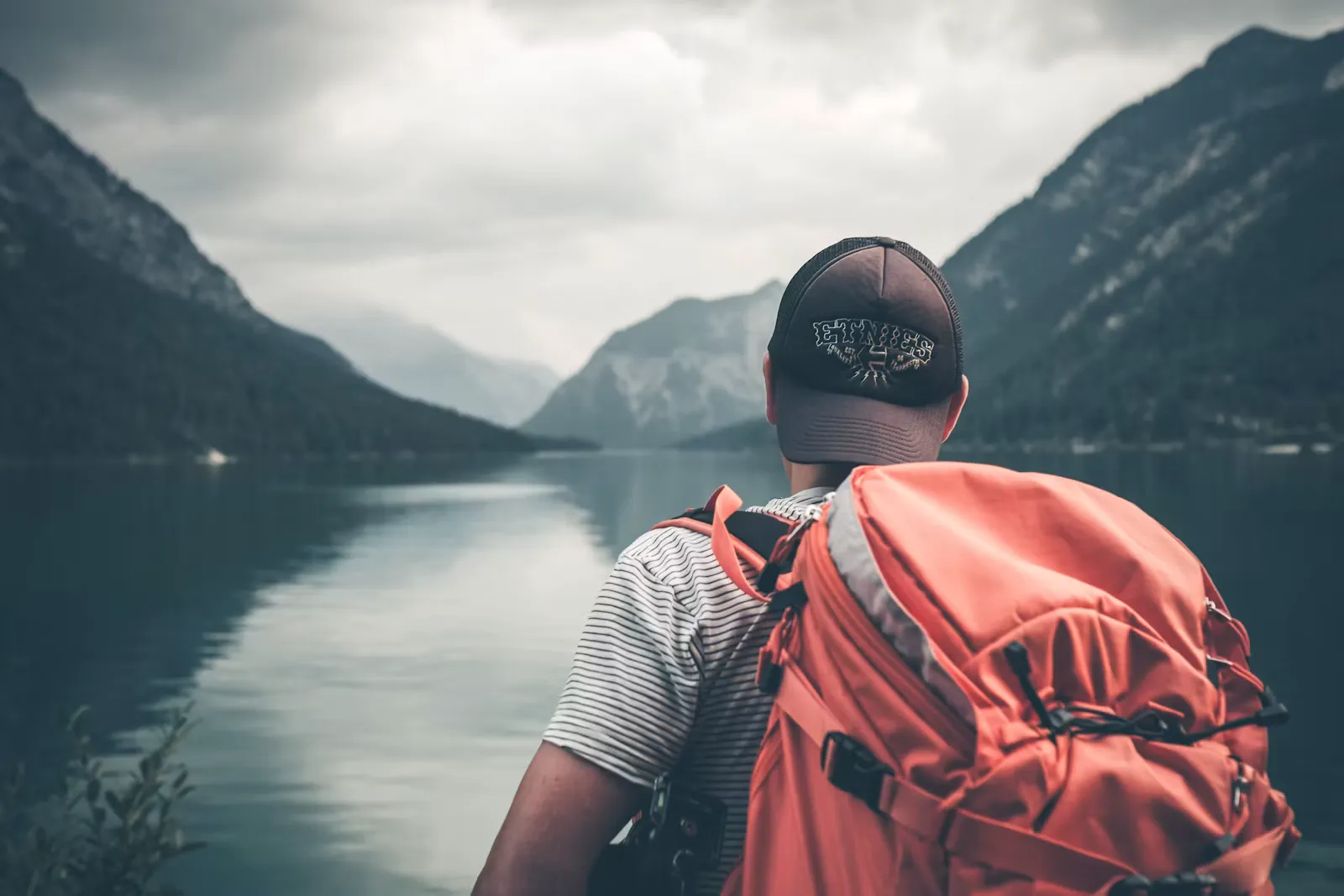 Reisender mit Rucksack blickt auf eine Berglandschaft, Symbol fuer die Reisezeit im Zwischenjahr nach der Matura