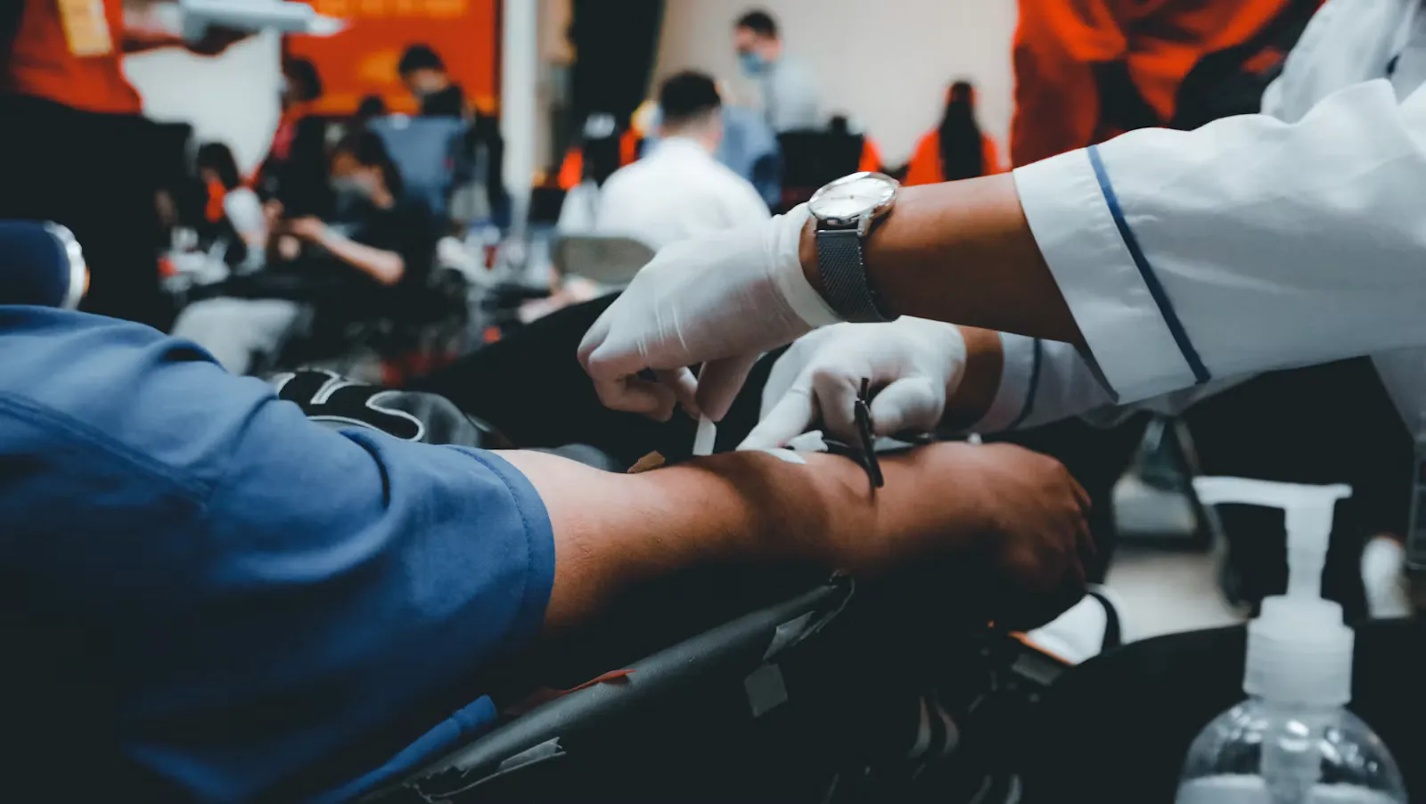 Gloved hands securing a needle in a patient's arm during a blood draw