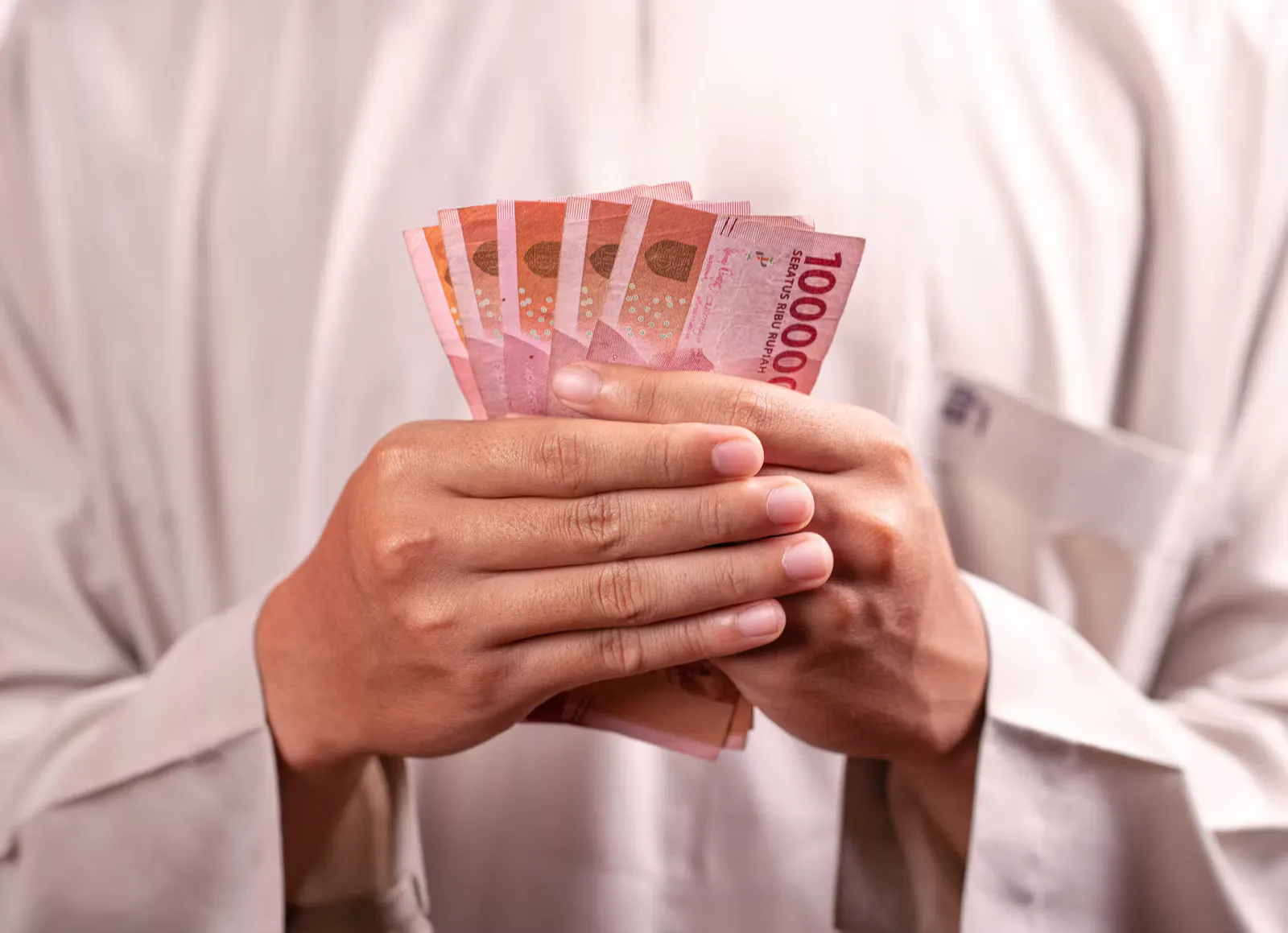Zwei Hände halten einen Fächer aus rosa 100'000-Rupiah-Scheinen vor einem hellen Hemd, Symbolbild für Bargeld auf Bali im Auslandspraktikum