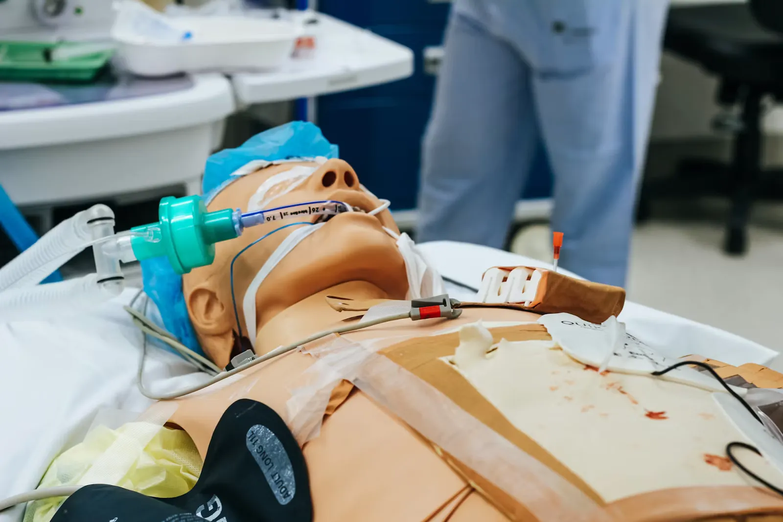 A resuscitation training manikin lying on a bed in a clinical simulation room