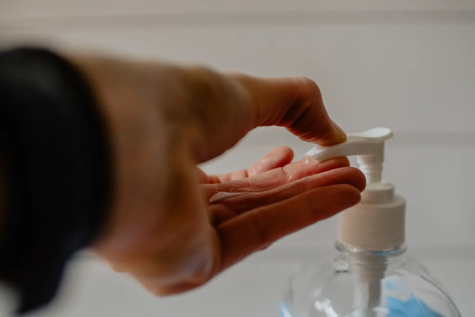 Hand greift nach einem Spender mit Händedesinfektionsmittel, Symbolbild für die fünf Momente der Handhygiene im Spital