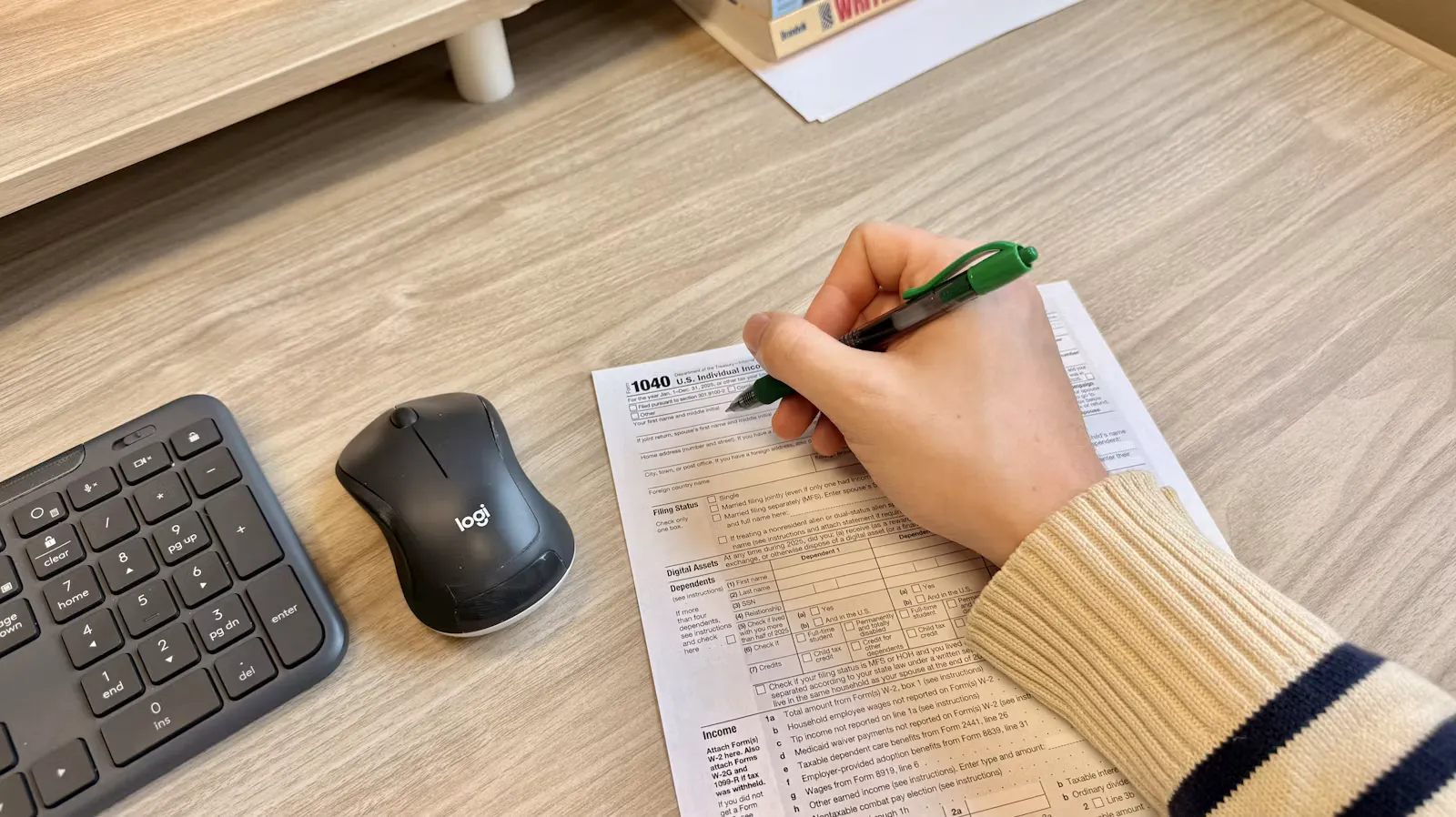 A hand writing on a printed document beside a keyboard and mouse on a desk