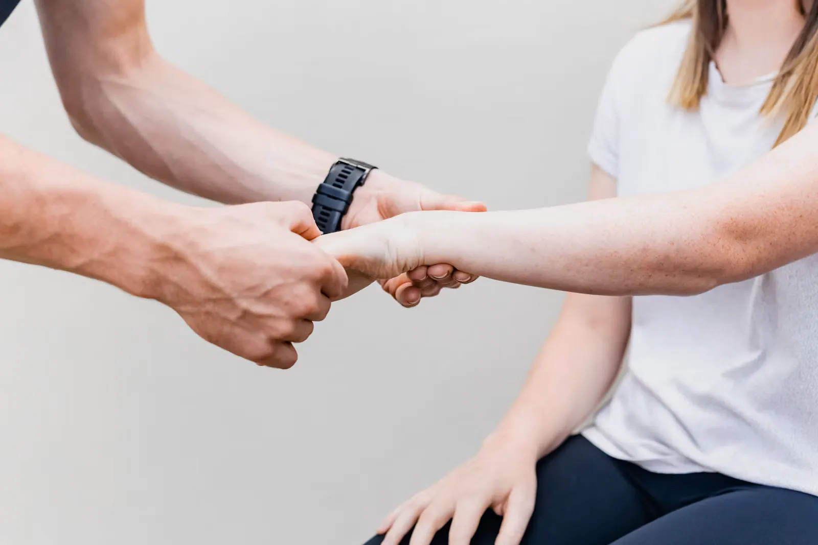 A therapist supporting the forearm and wrist of a seated patient during a rehabilitation exercise after a stroke