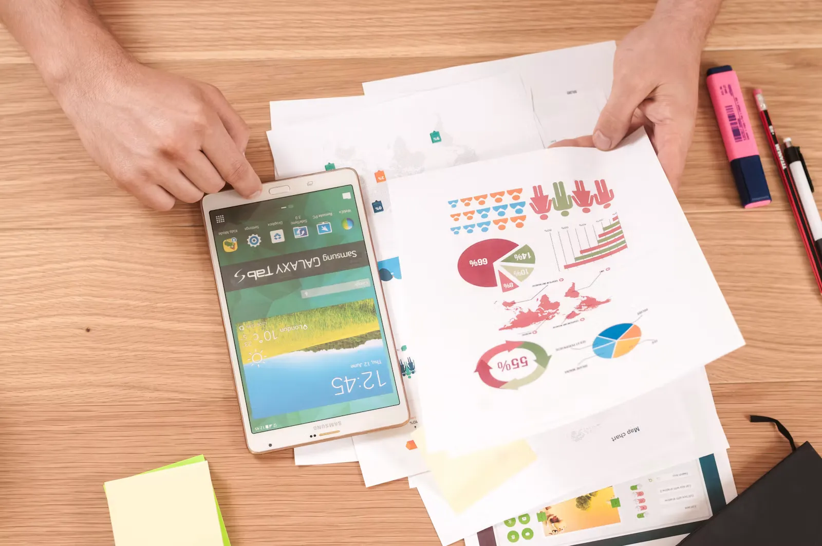 Hände über Schreibtisch mit ausgedruckten Diagrammen, Statistiken, Tablet und Textmarker, Symbolbild für die Auswertung von Zulassungszahlen