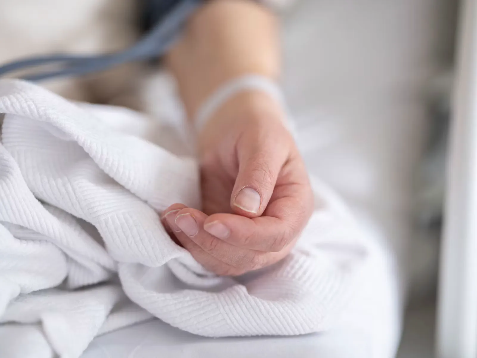 Hand einer Patientin mit Patientenarmband auf einer weißen Krankenhausdecke, Symbol für Pflege im Krankenhaus bei der Freiwilligenarbeit auf Sansibar