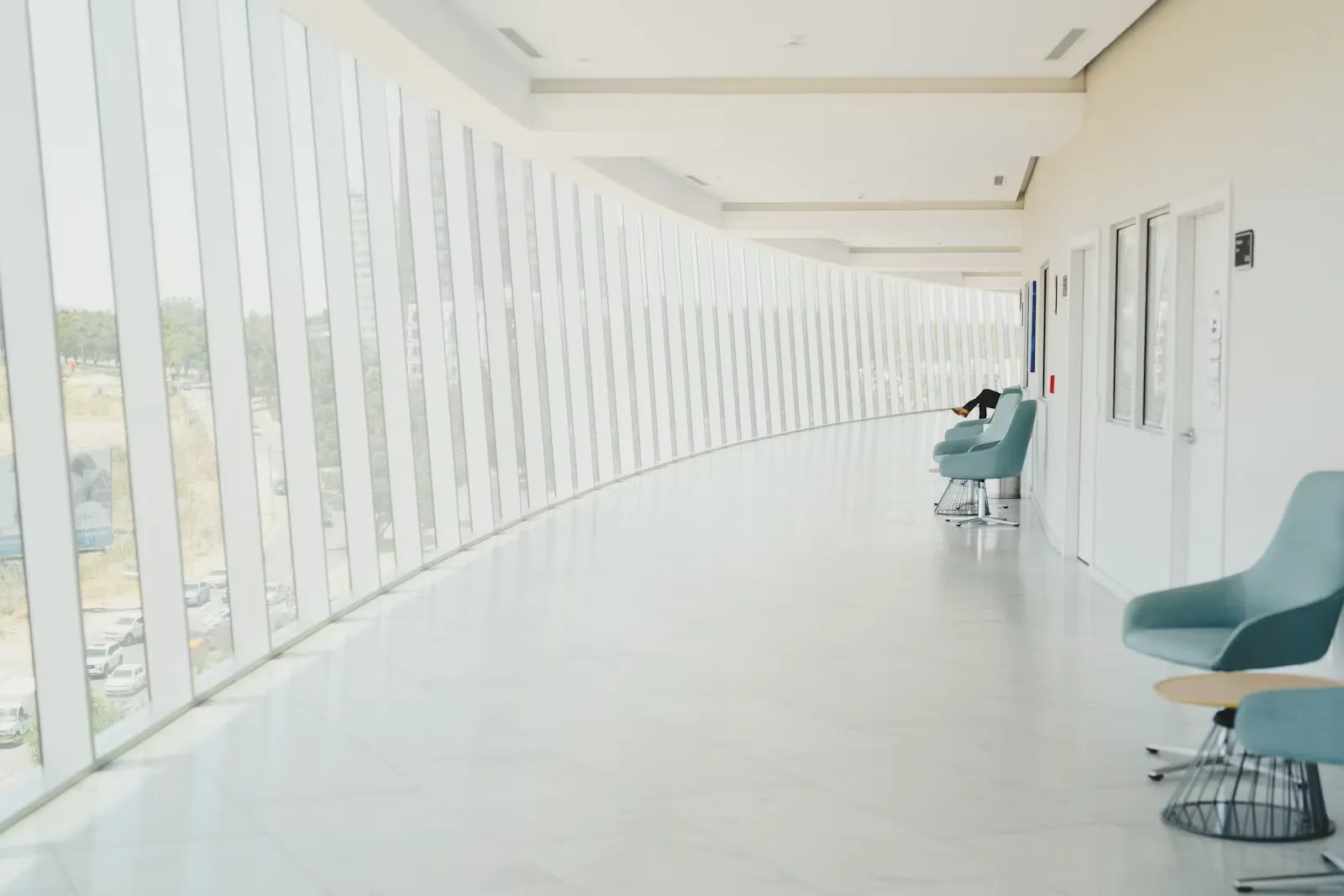 Bright curved hospital corridor with a glass facade and turquoise waiting chairs