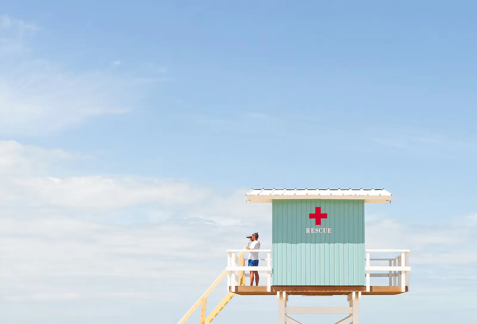 Lifeguard rescue hut with a red cross on a pale blue sky with summer clouds