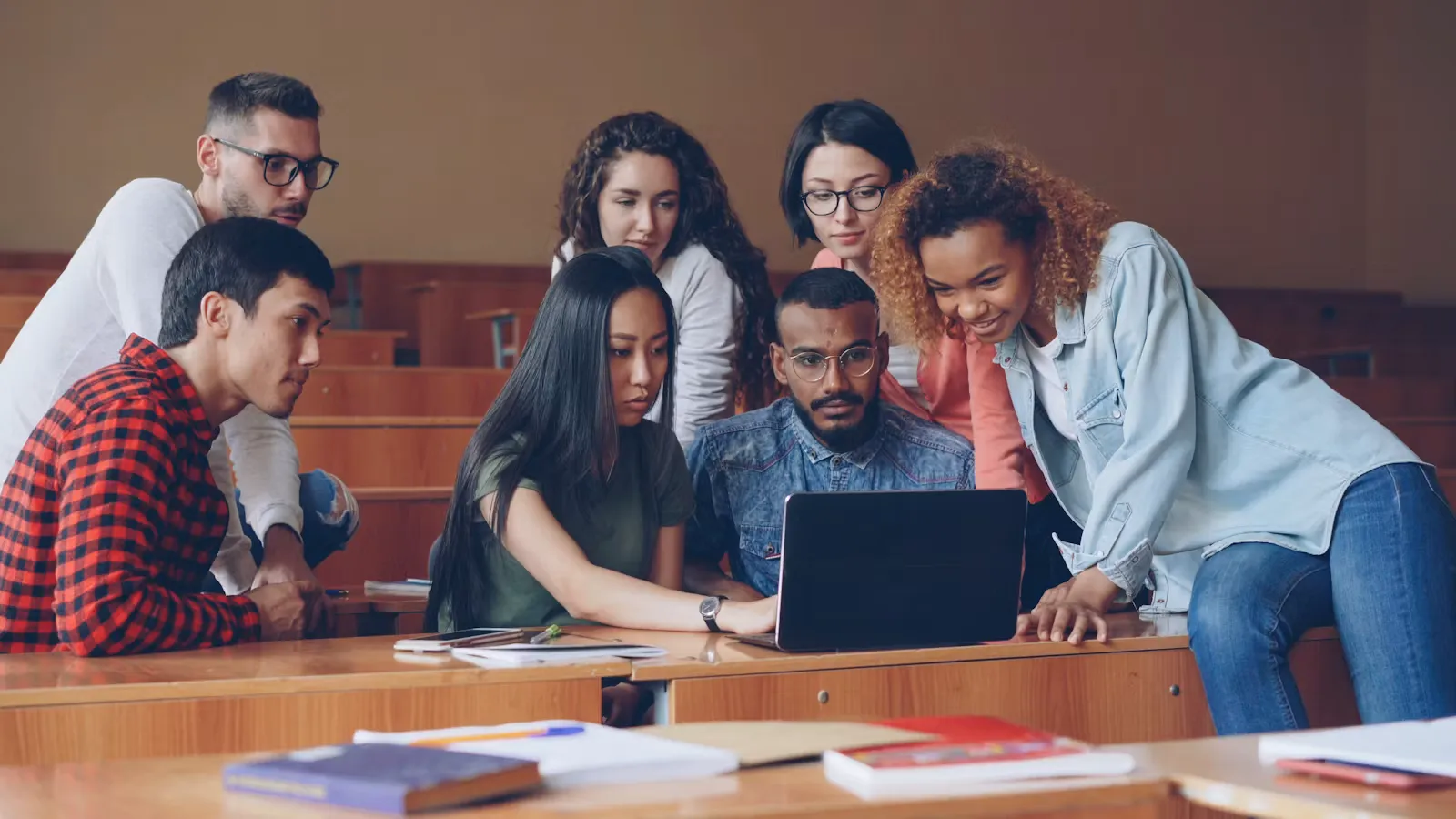 Group of students gathered around a laptop in a lecture hall