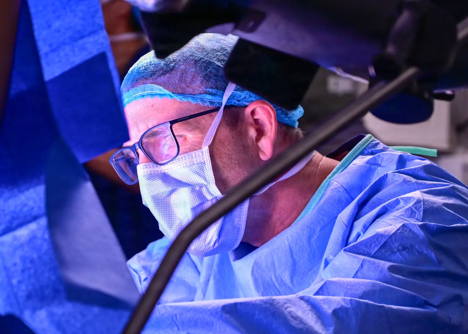 A surgeon in blue scrubs, mask and cap operating