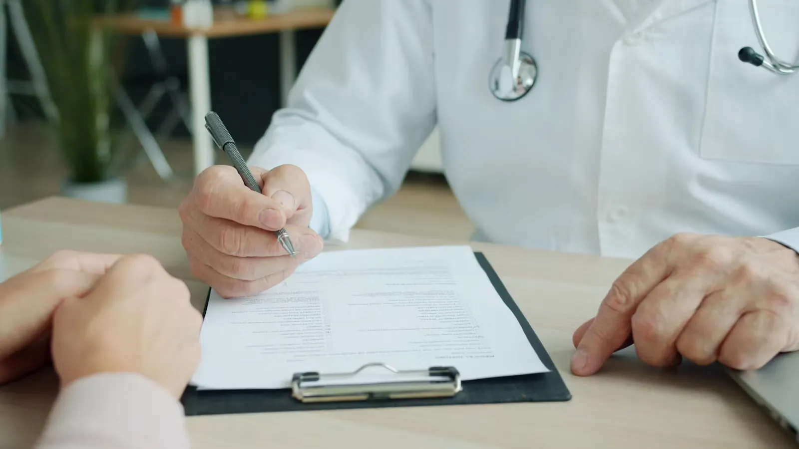 Doctor writing notes on a patient's chart, representing the hands-on supervised work that produces a strong reference letter for a residency application