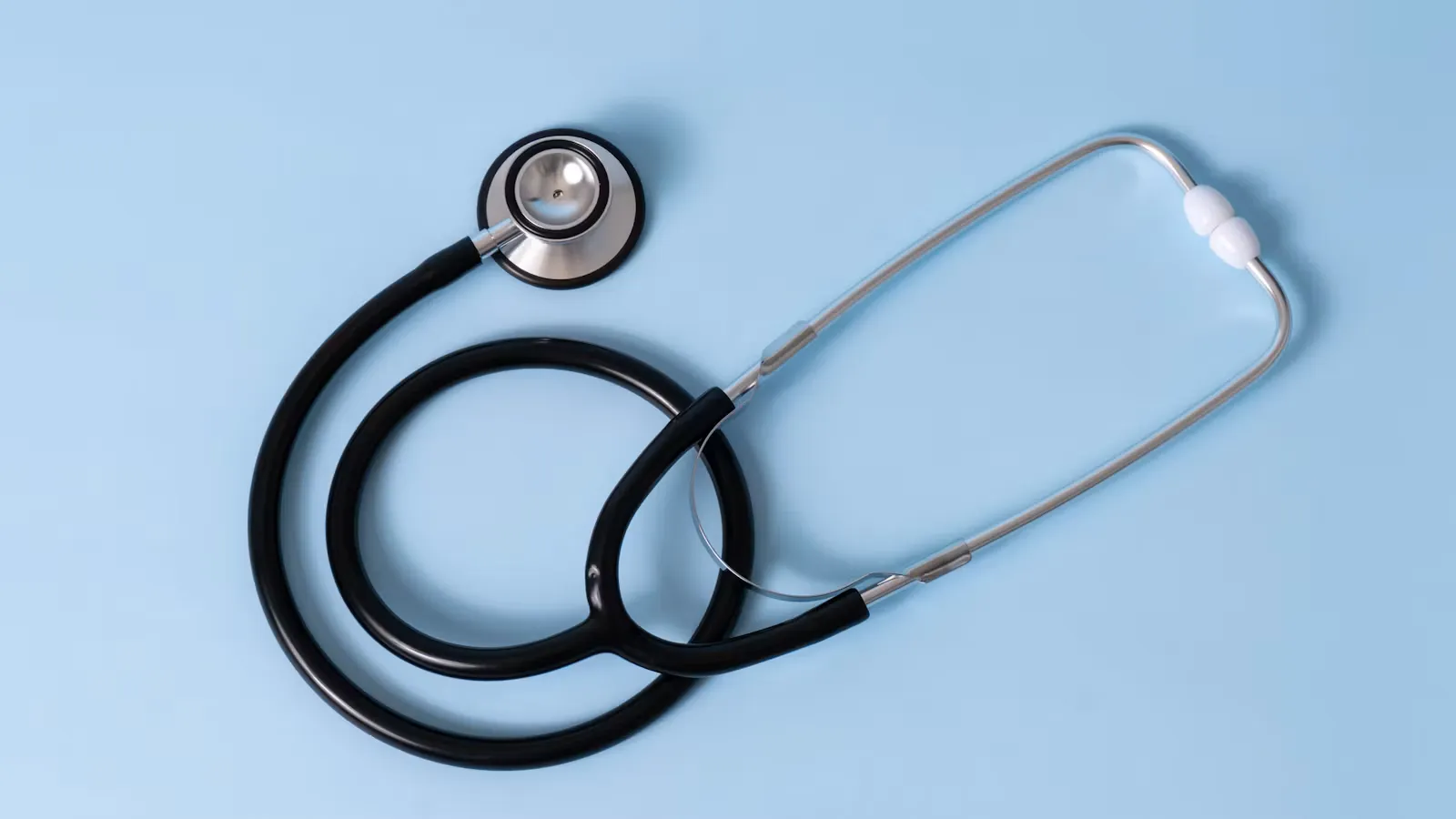 A black medical stethoscope photographed on a light blue background