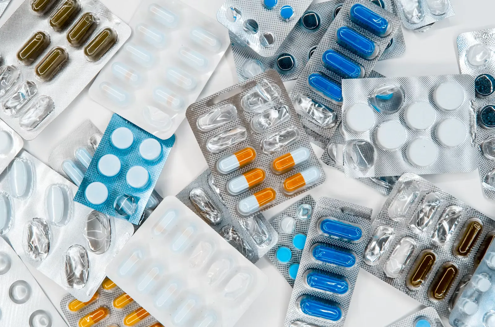 Viele angebrochene Tablettenblister mit blauen, weißen und orangen Tabletten und Kapseln auf hellem Untergrund, Symbolbild für Selbstmedikation mit Antibiotika im Auslandspraktikum
