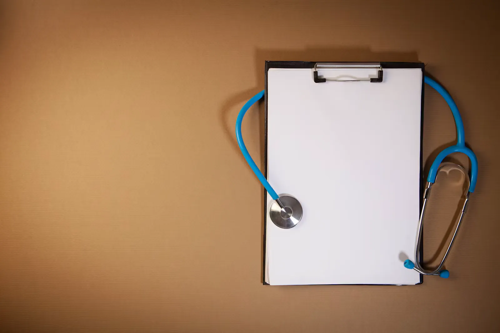 A clipboard holding lined paper next to a stethoscope on a brown surface