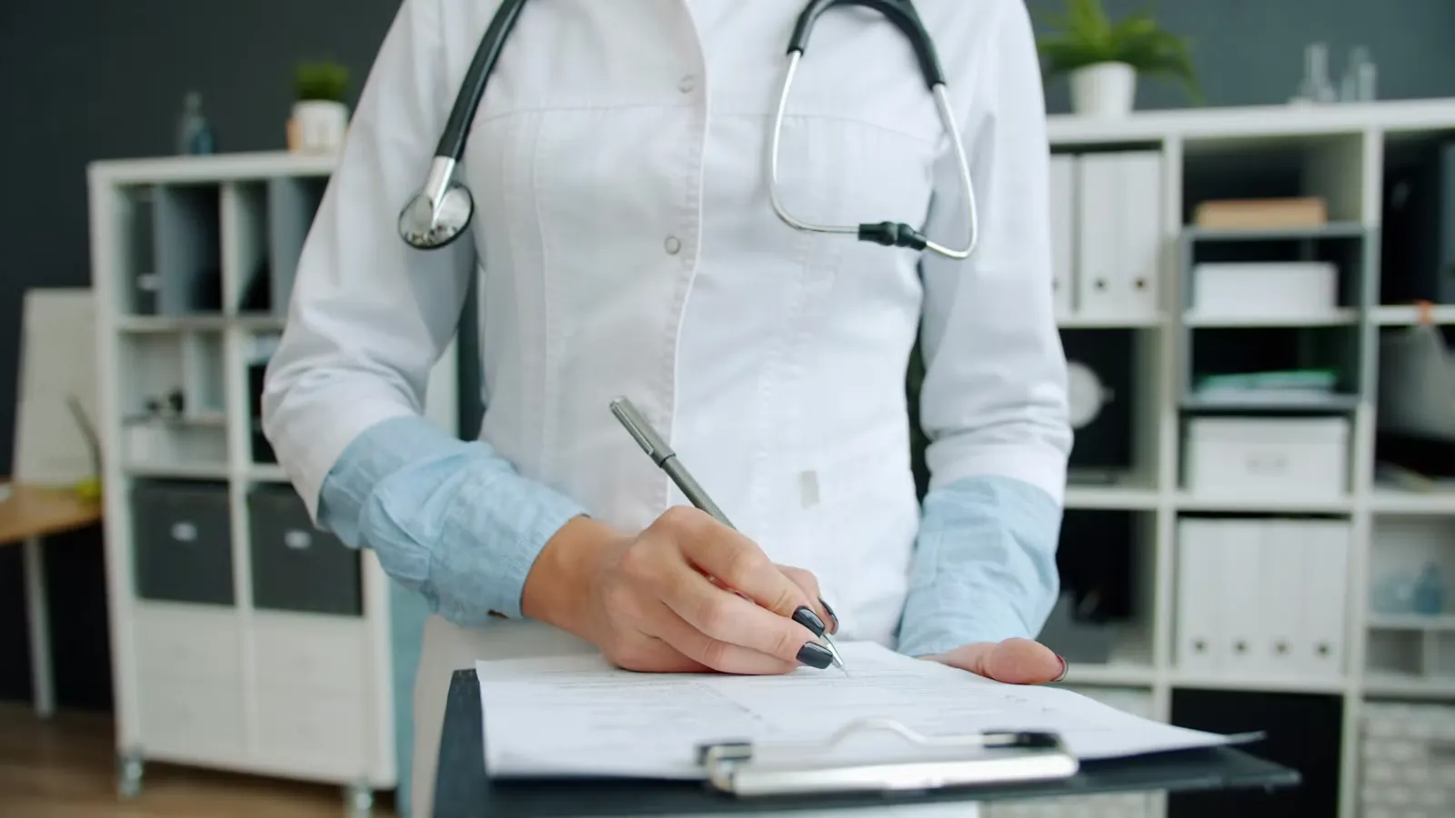 Close-up of a clinician's hand writing on a clipboard in an office, representing a supervisor drafting a reference letter for a medical elective abroad