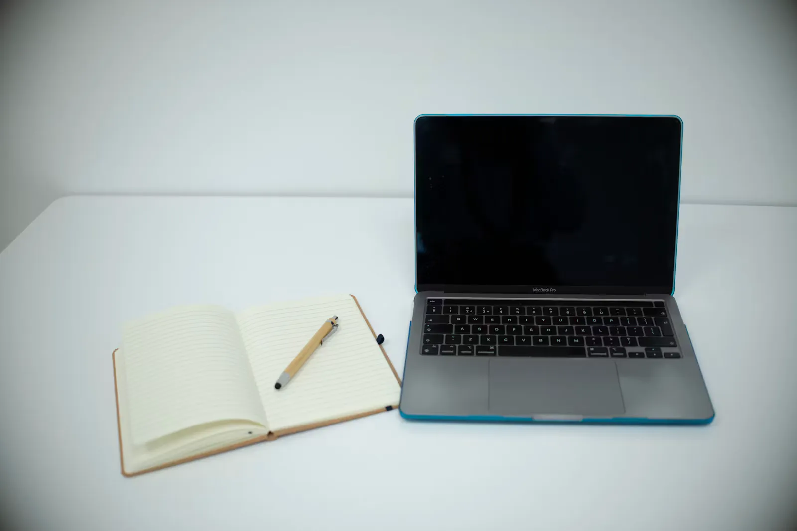 An open lined notebook with a bamboo pen lying next to an open laptop on a white desk
