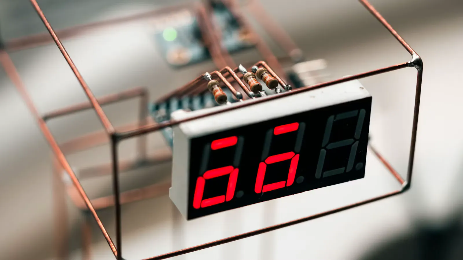 Red seven segment display wired with bare copper wires and banded resistors inside a wire frame, a small working circuit like the ones in current electricity