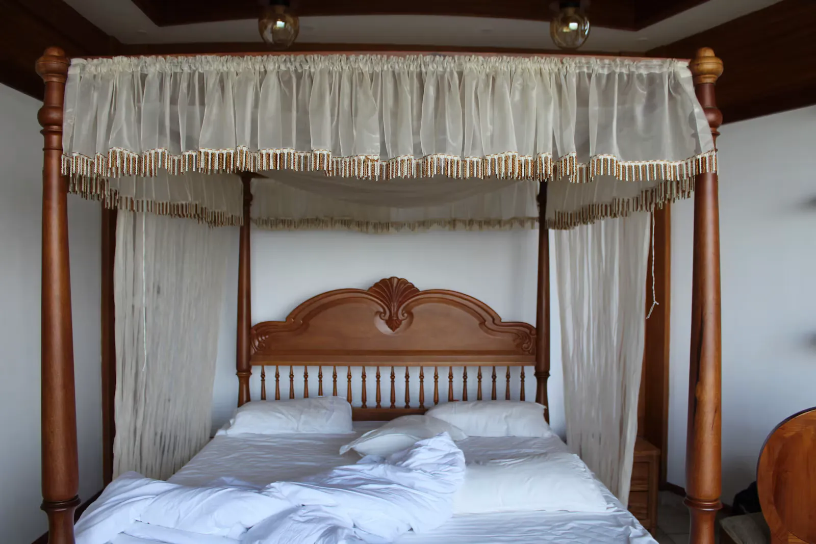 Himmelbett aus dunklem Holz mit hellen Vorhängen und weißer Bettwäsche in einem schlichten Zimmer, Beispiel für ein Zimmer mit Netz im Auslandspraktikum