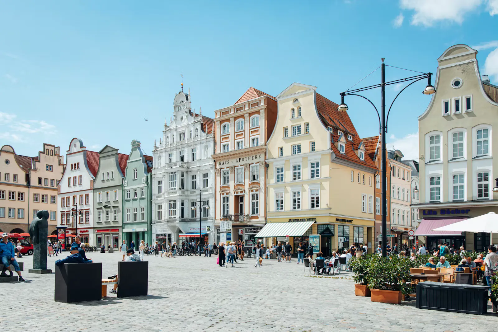 Bunte Giebelhäuser und Straßencafés auf einem sonnigen Altstadtplatz mit Kopfsteinpflaster