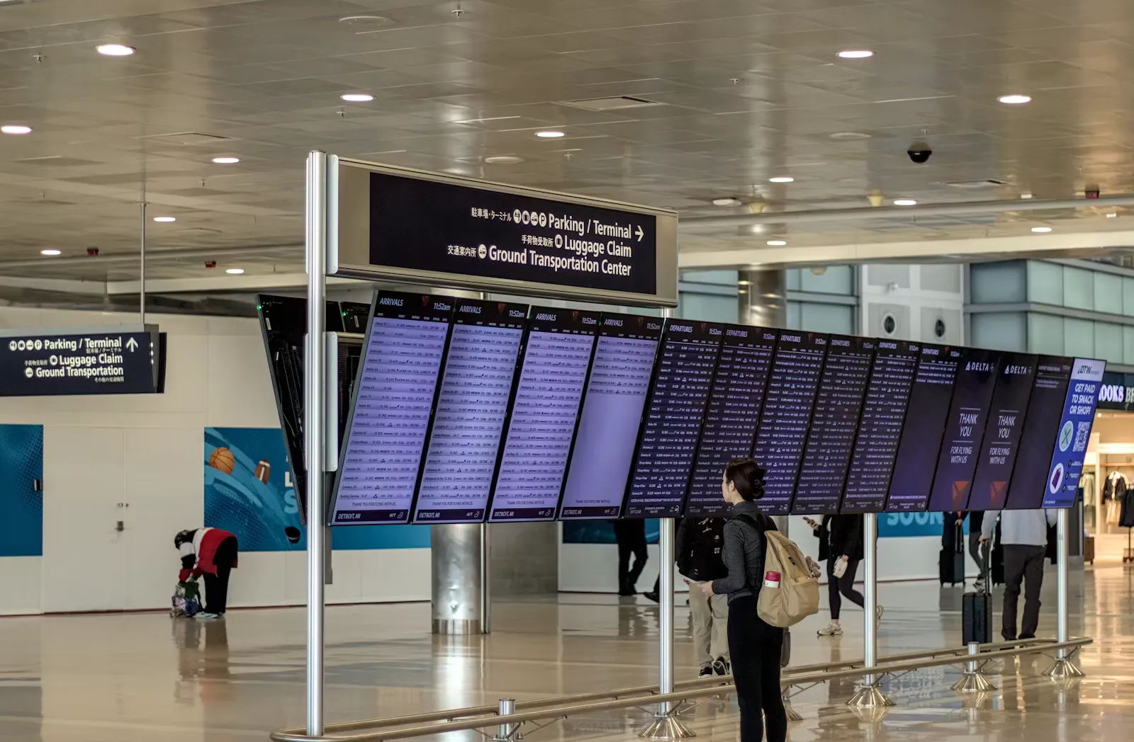 Person mit Rucksack steht vor einer grossen Anzeigetafel mit Flugdaten in einer Flughafenhalle