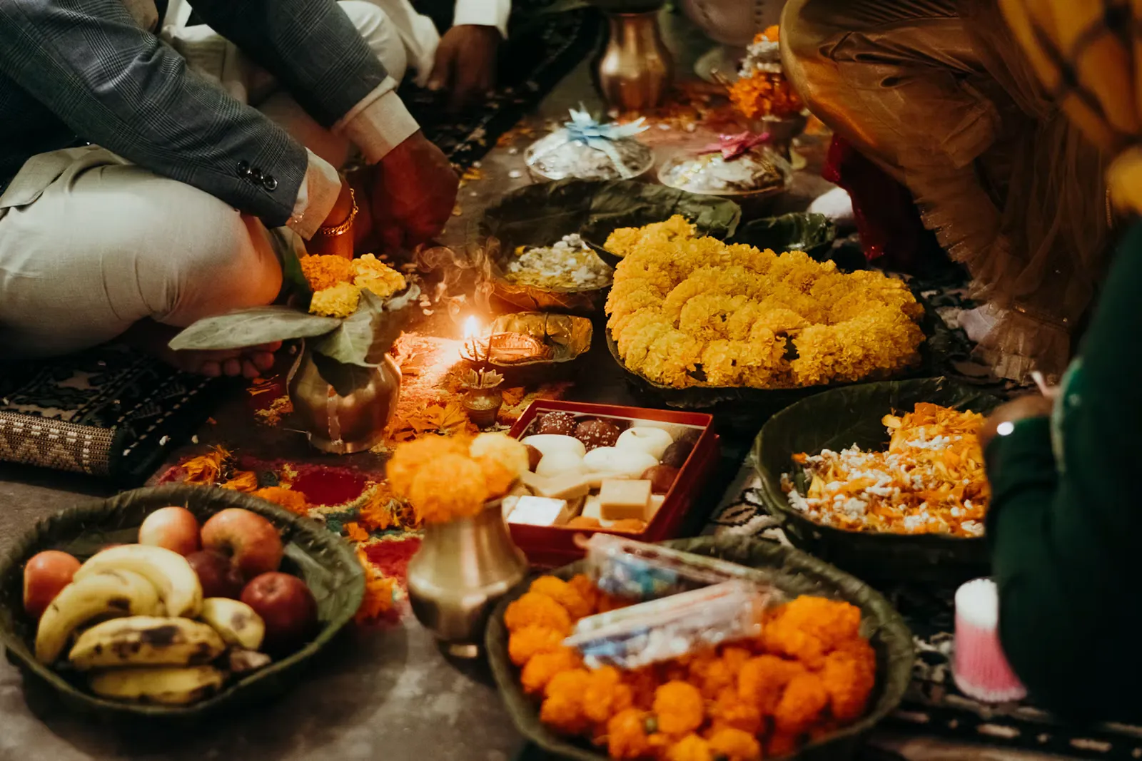 Plates of festival food and marigold flowers arranged around a small oil lamp for a puja ceremony