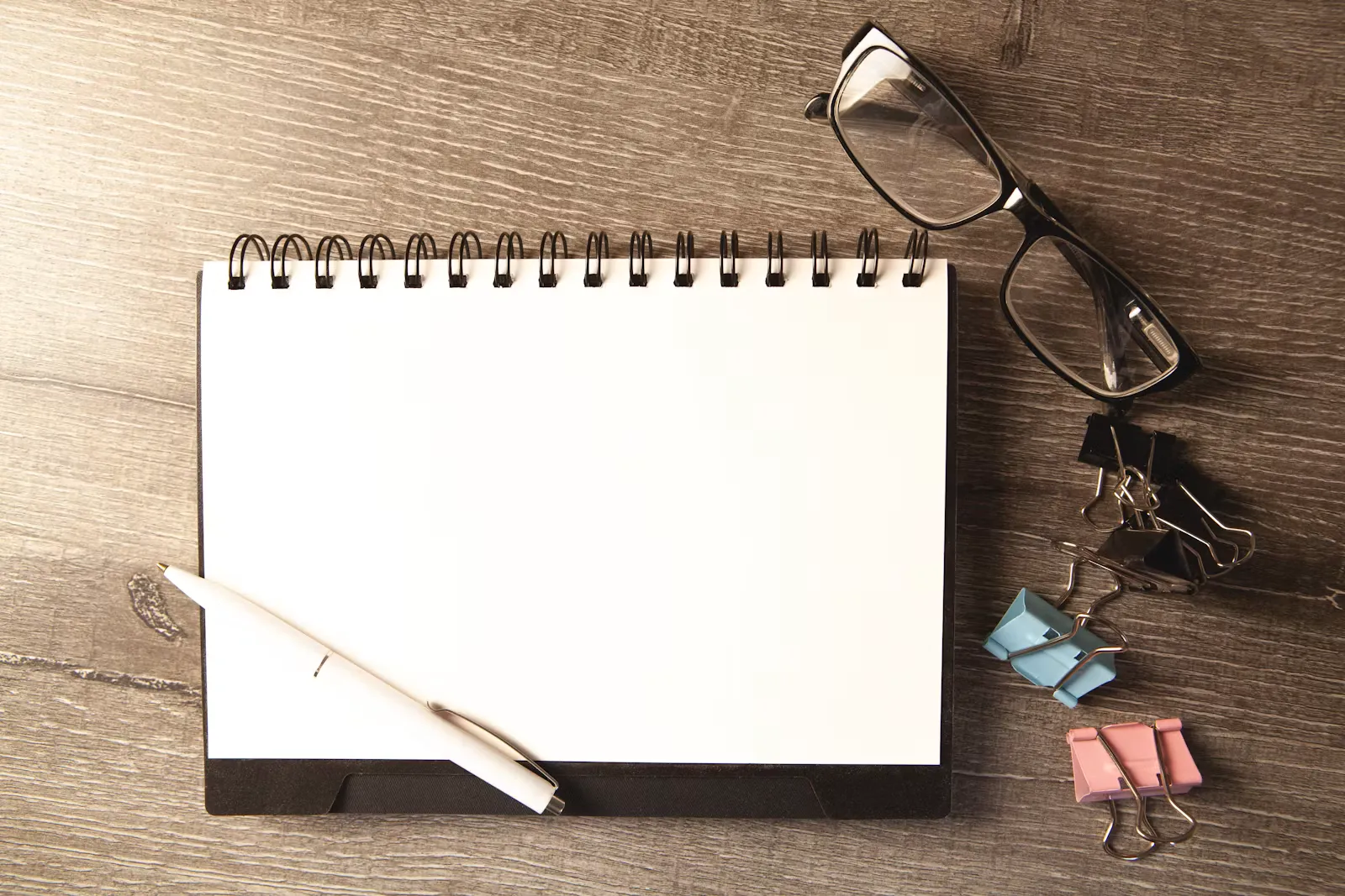 Schreibtisch mit Notizblock, Stift, Brille und Büroklammern