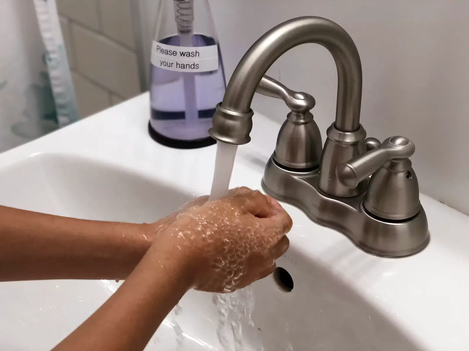 Hände werden mit Seife unter fließendem Wasser an einem weißen Waschbecken gewaschen