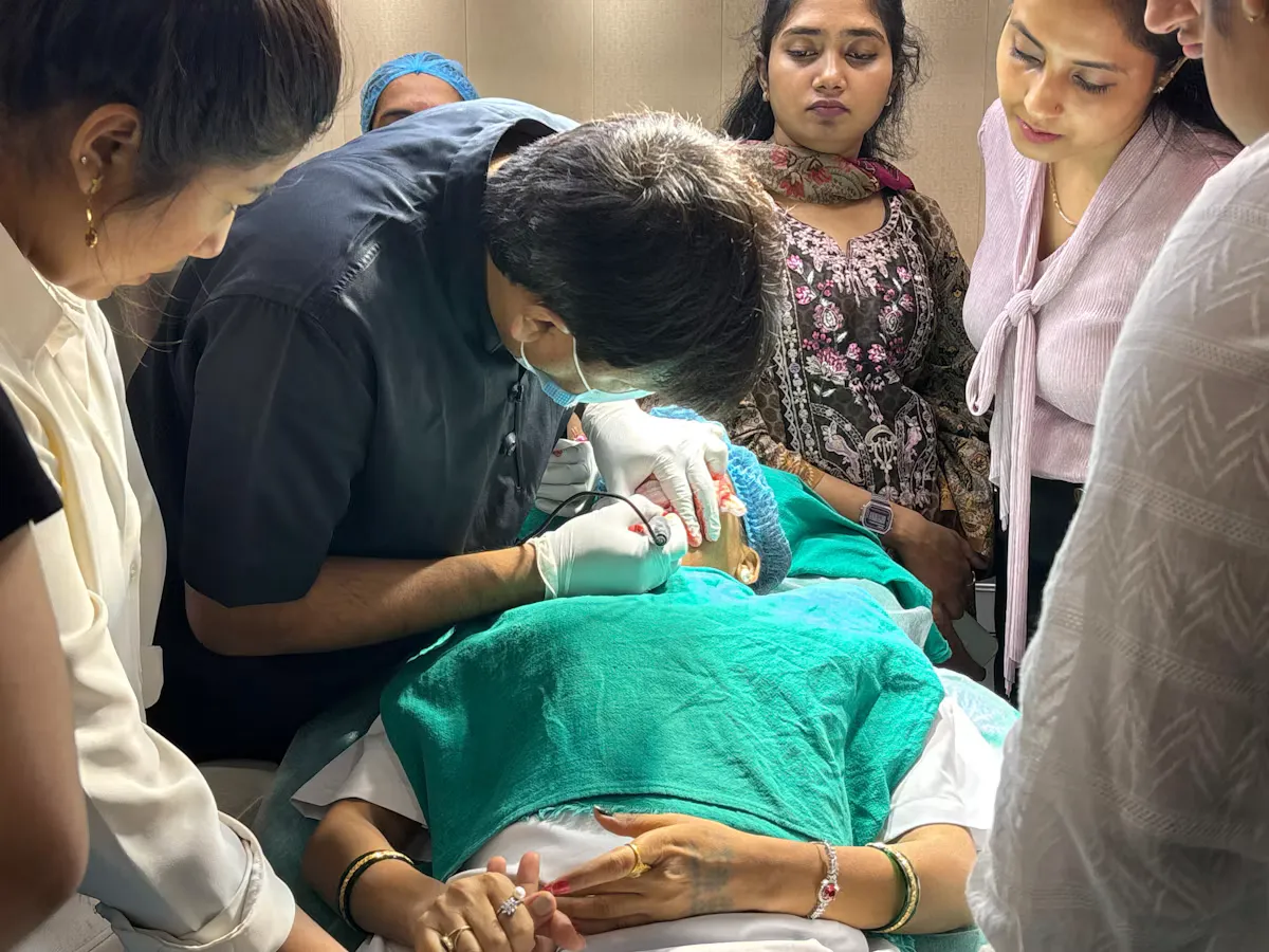 A doctor in gloves and a mask performs a procedure on a patient while a group of doctors watches and learns