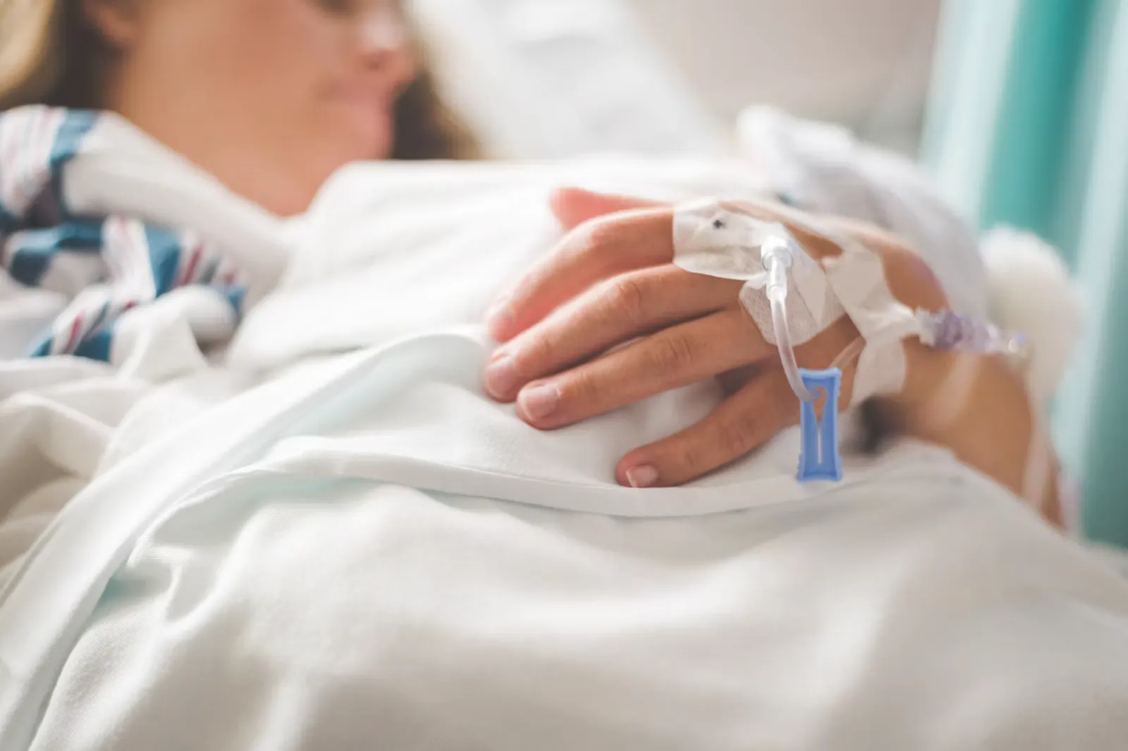 A patient resting in a hospital bed with a cannula taped to the back of one hand