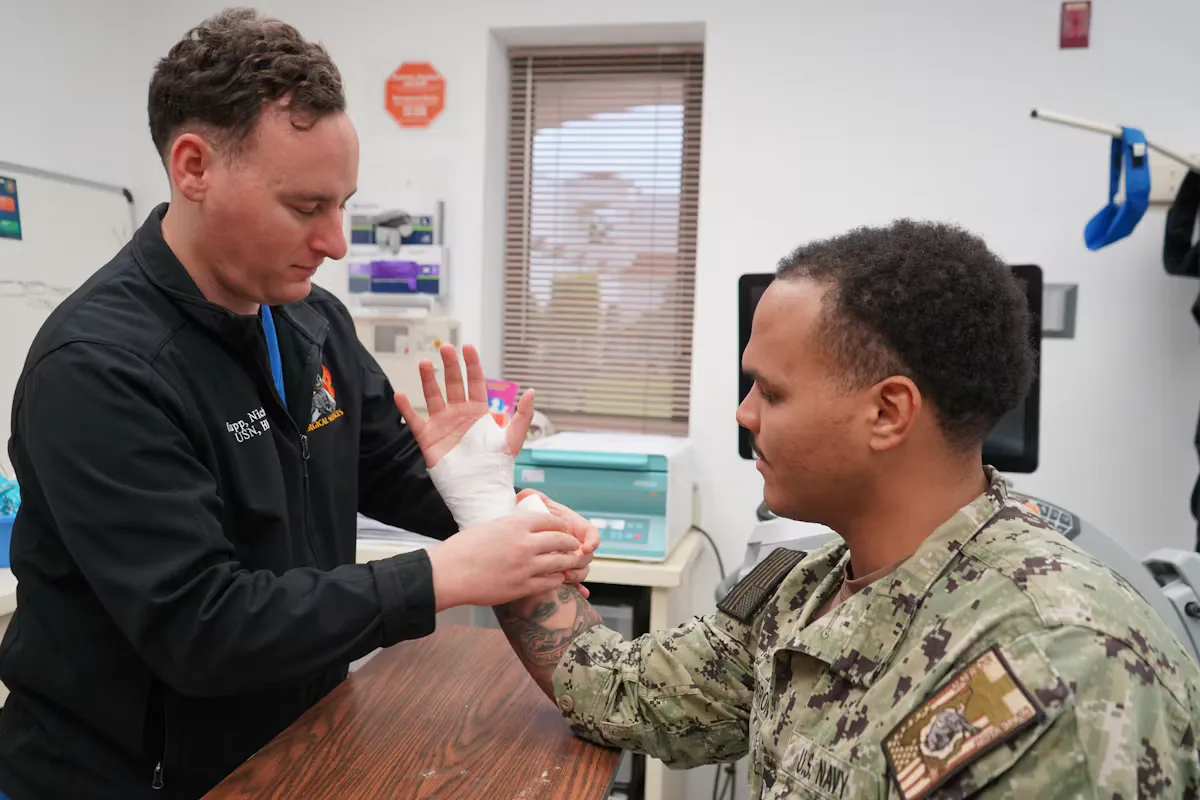 A medical professional bandaging the hand of a uniformed service member in a bright military clinic