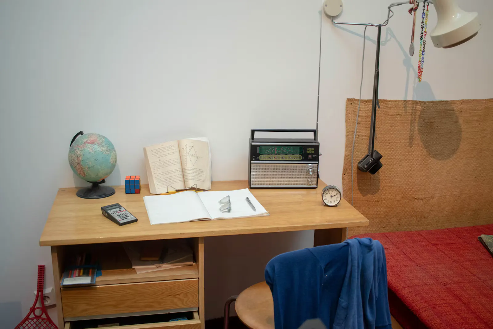 Schlichtes Studentenzimmer mit Holzschreibtisch, Globus, aufgeschlagenem Buch, Radio und einem Stuhl mit blauer Jacke, Sinnbild für ein WG-Zimmer, das während des Auslandspraktikums untervermietet wird
