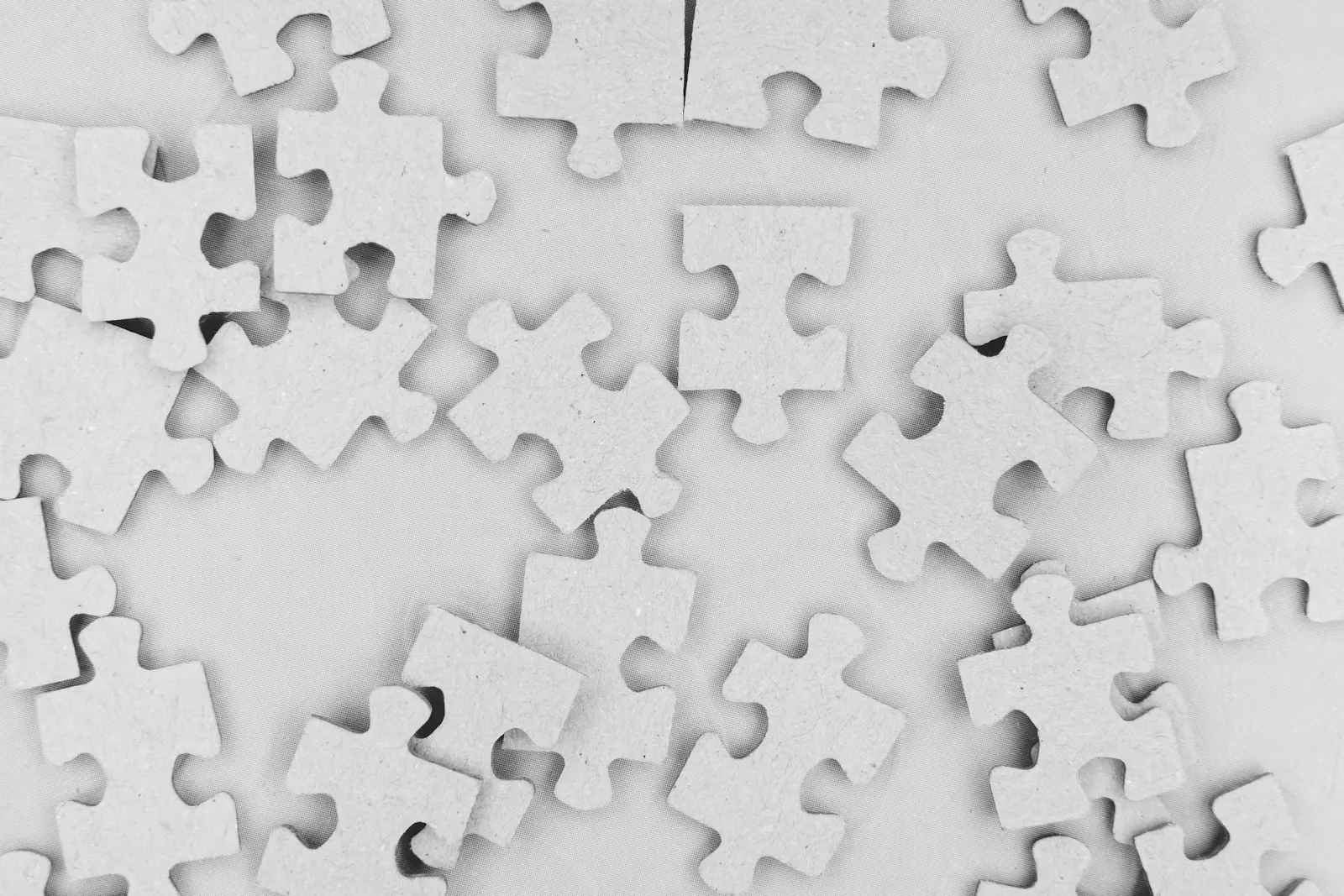 Graue Puzzleteile aus Pappe lose verstreut auf einer hellen Fläche, Sinnbild für Regel- und Raumaufgaben in der PhaST Vorbereitung