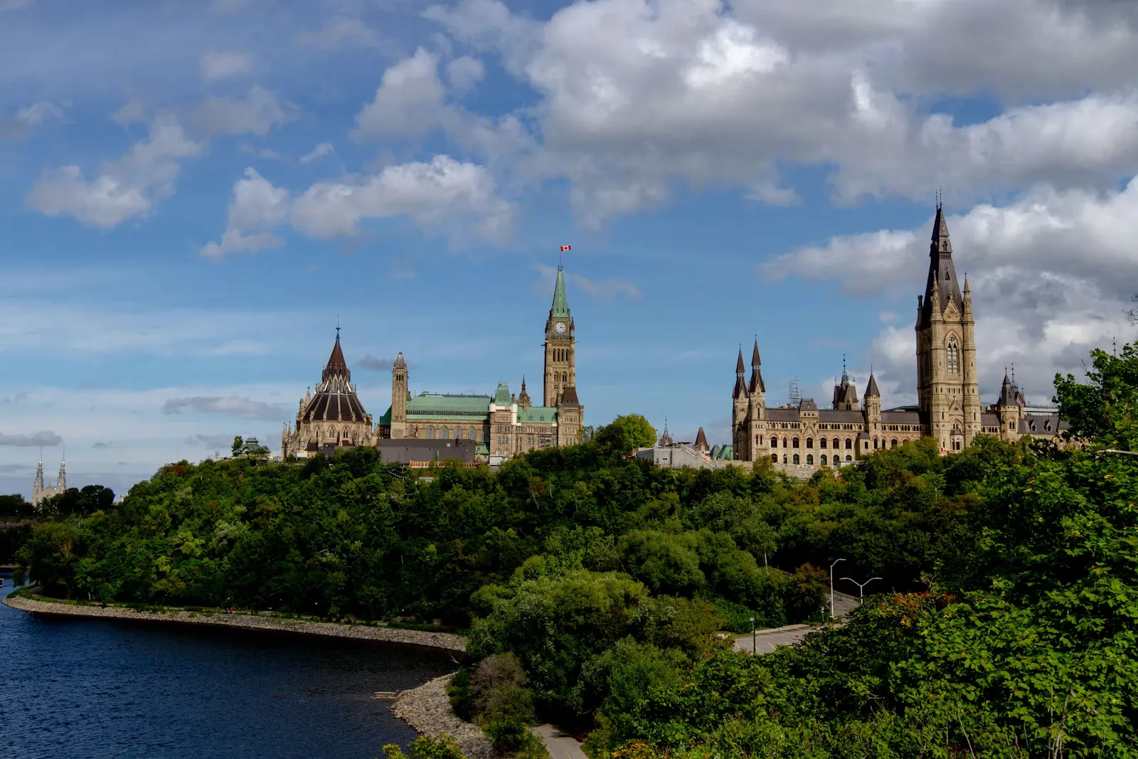 A stone Canadian government building framed by green trees under a clear blue sky