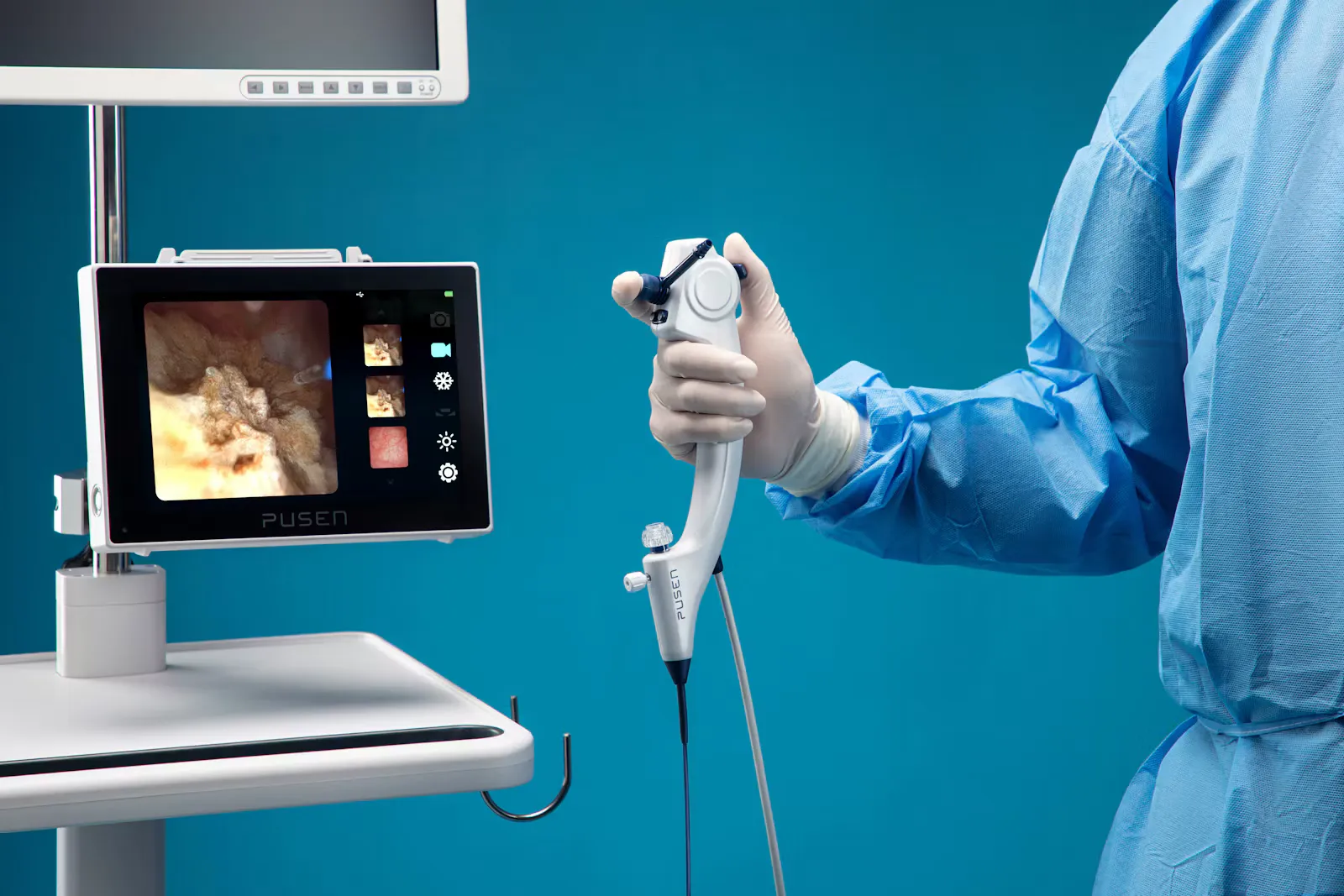 A doctor in a blue sterile gown holding the handle of a single-use flexible scope next to a video monitor showing the live camera view