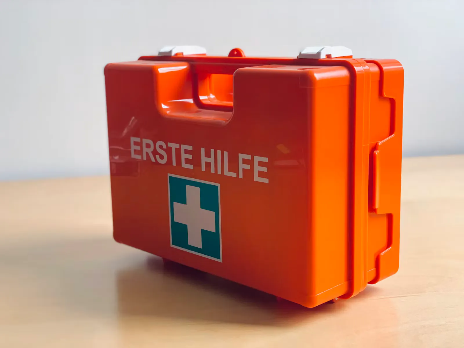 Oranger Erste-Hilfe-Koffer mit weissem Kreuz auf grünem Feld steht auf einem hellen Holztisch, Symbolbild für die Wundversorgung und die Tetanus-Impfung im Auslandspraktikum