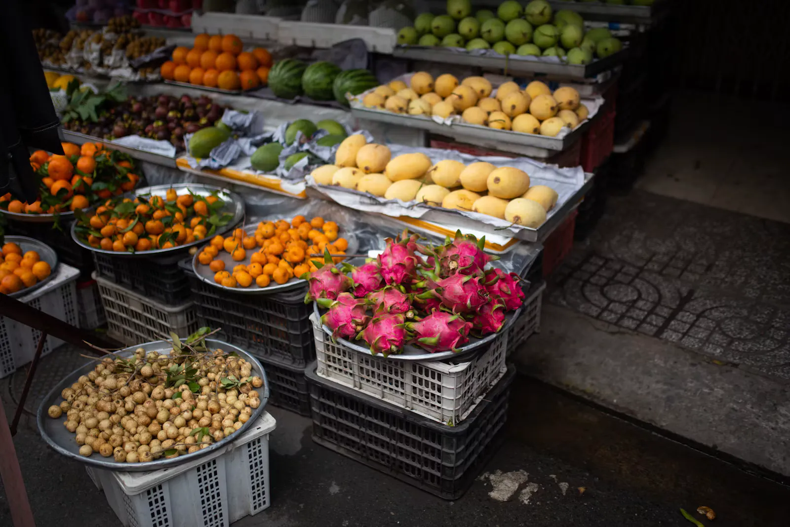 Marktstand mit Drachenfrüchten, Mangos, Mandarinen und Longan in Plastikkisten am Strassenrand, typische Lebensmittel, bei denen die Hepatitis-A-Impfung und Hygiene schützen