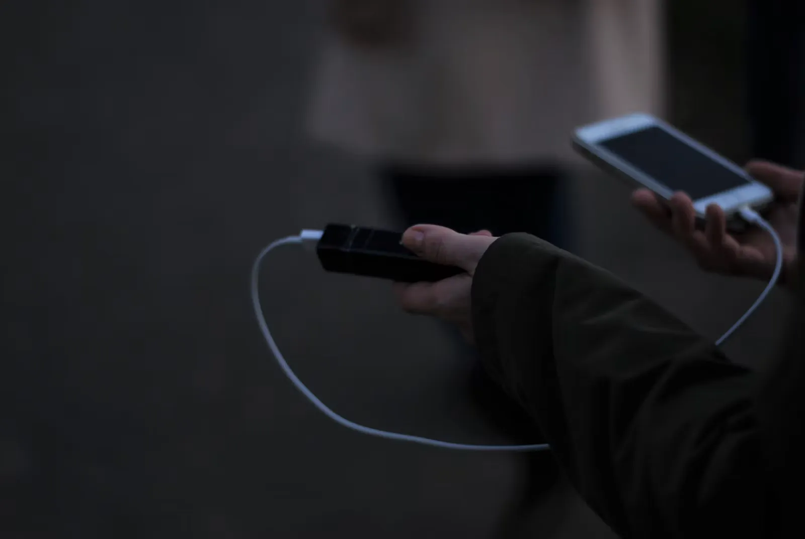 Hand hält ein Mobiltelefon und ein Ladekabel über einer hellen Tischplatte, Symbolbild für das Laden von Geräten auf einer Flugreise