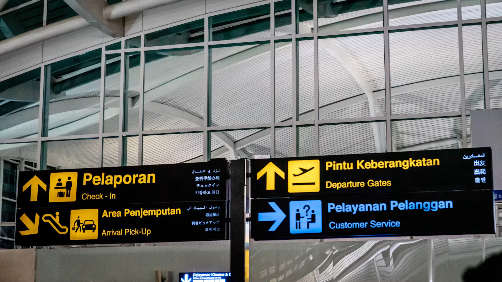 Yellow and black signs at Bali's airport pointing to check in, arrival pick up, departure gates and customer service in Indonesian and English