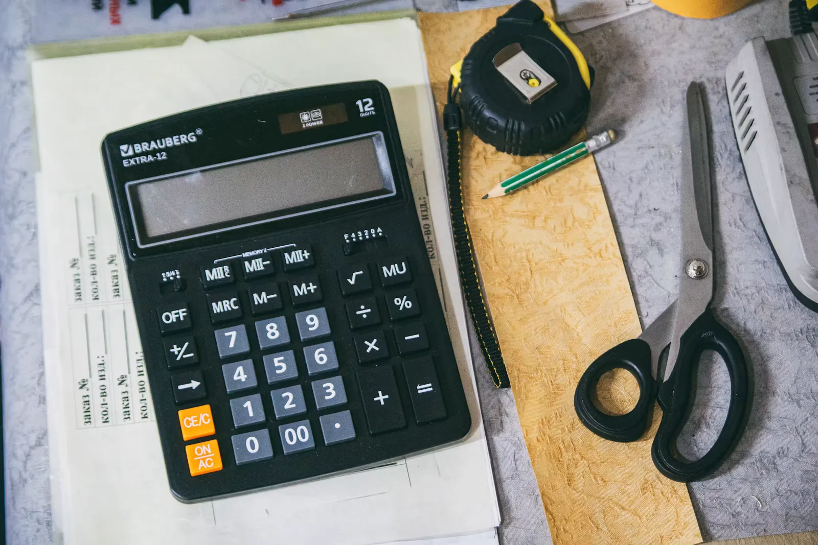 Taschenrechner, Notizblock und Büromaterial auf einem hellen Schreibtisch