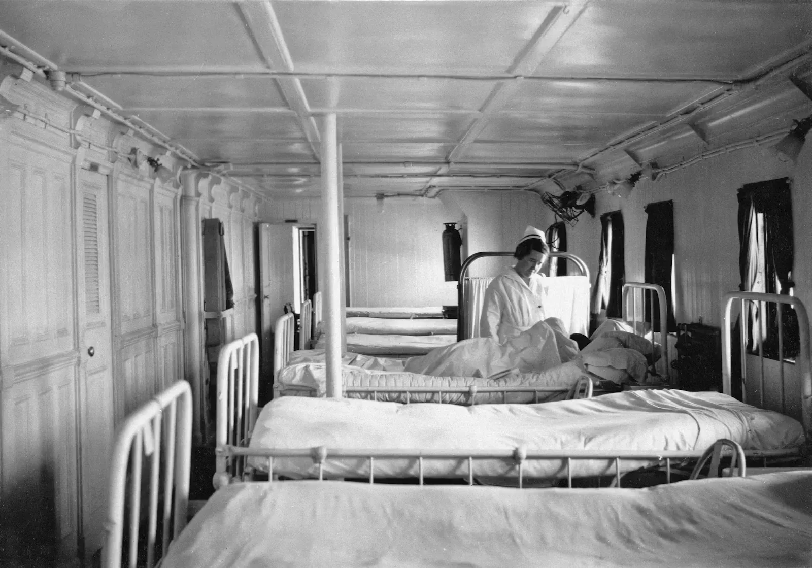 A nurse attending to a patient in a hospital ward lined with beds