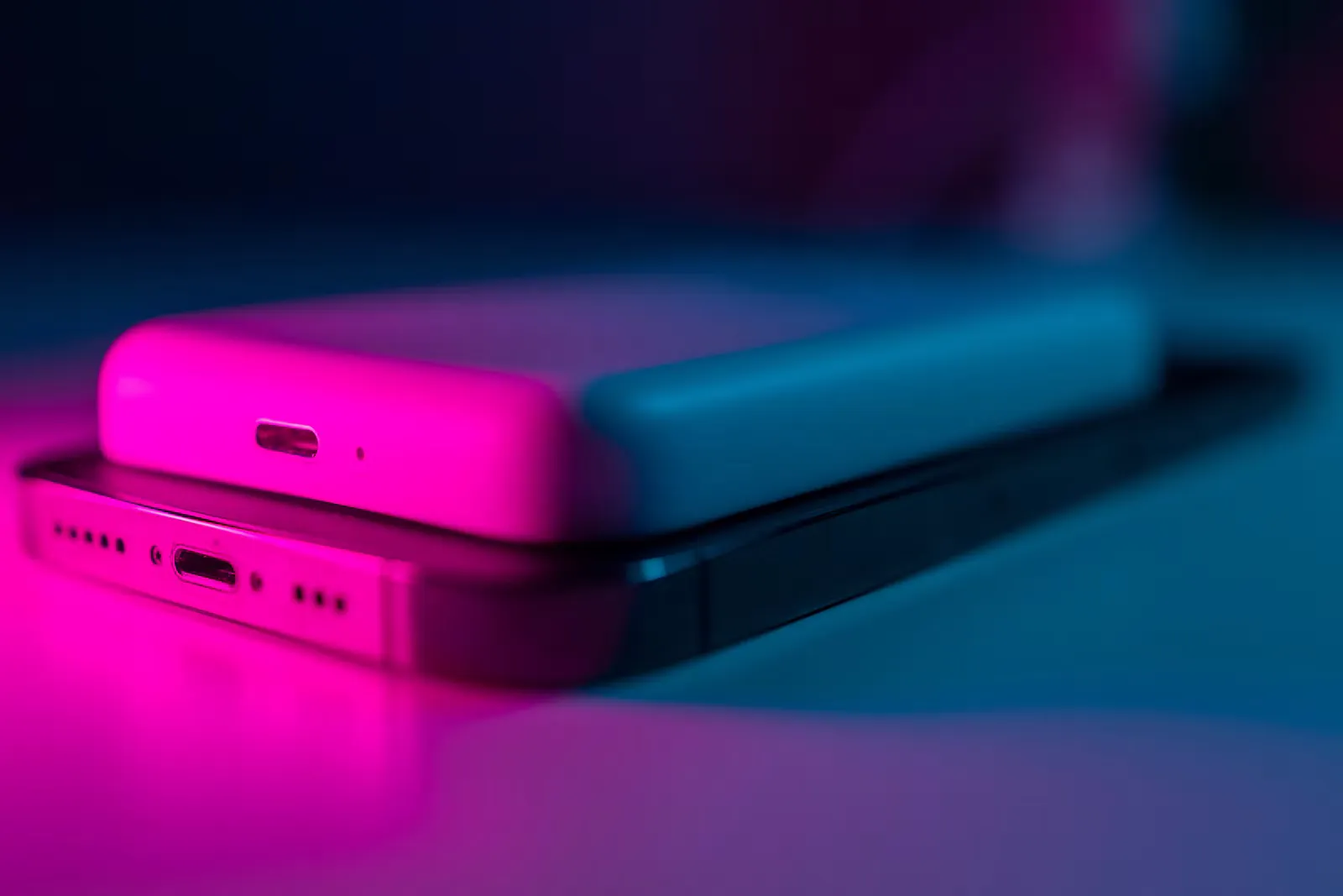 Weiße kabellose Powerbank liegt magnetisch auf der Rückseite eines Smartphones, in pinkes und blaues Licht getaucht