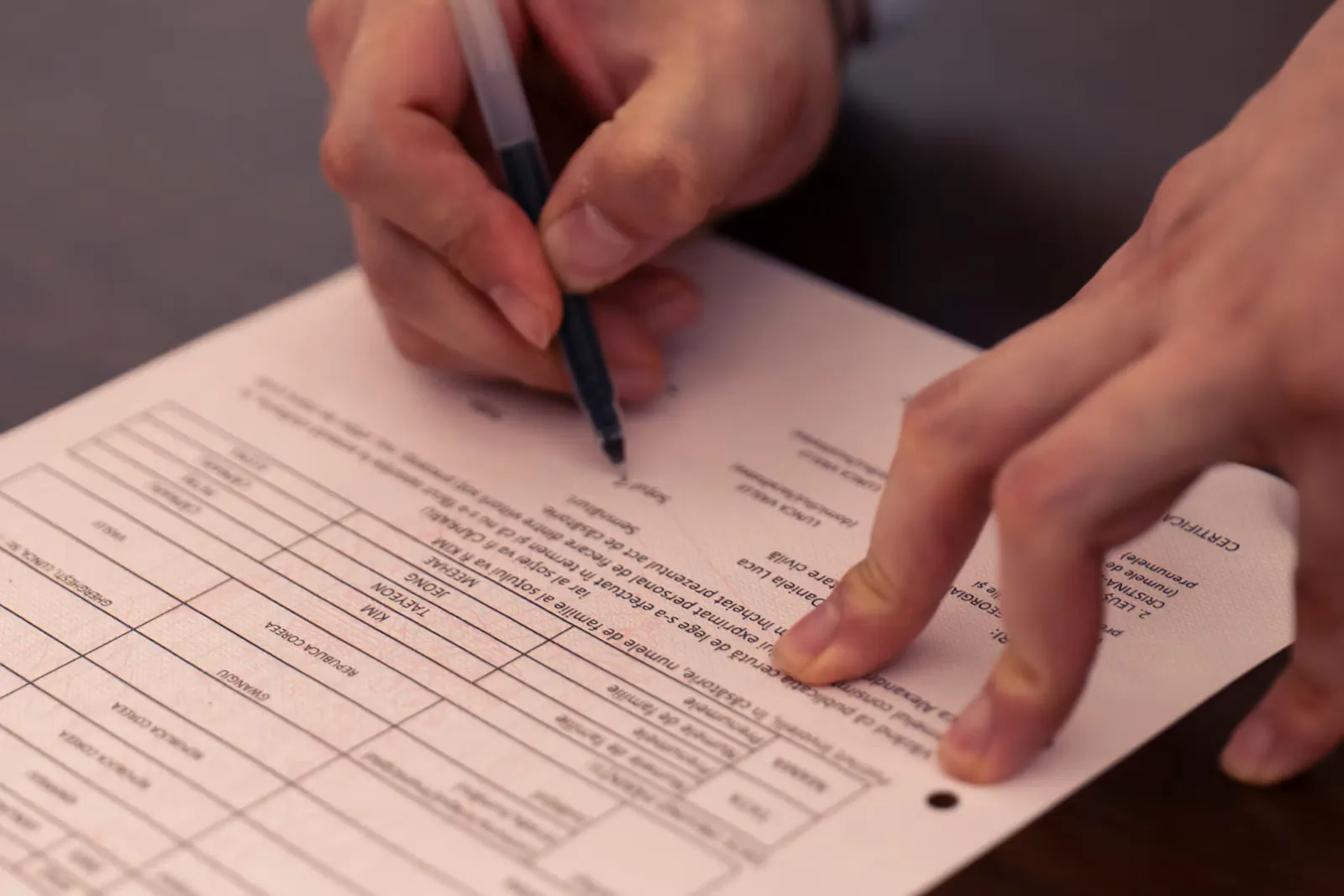 Hands filling in an official application form with a pen on a dark desk