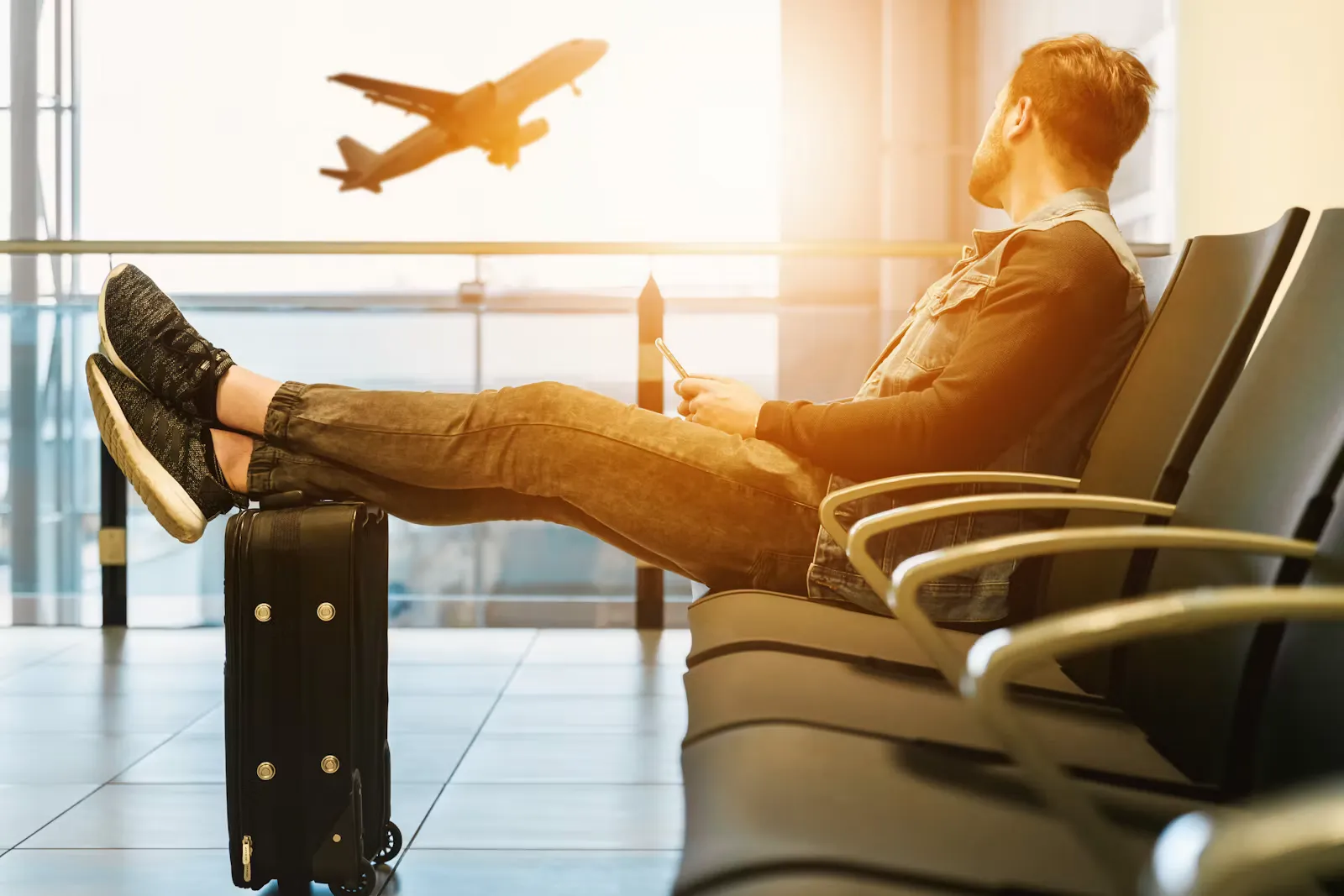 A young traveller waiting in an airport departure lounge with a suitcase as a plane takes off outside the window — the day the residence permit clock starts