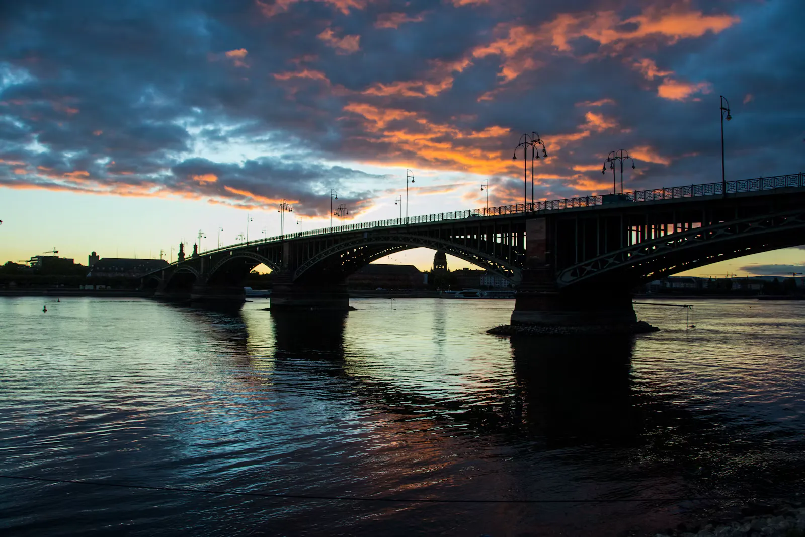 Bogenbrücke über den Rhein bei Sonnenuntergang, der Himmel in Orange und Dunkelblau spiegelt sich im Wasser