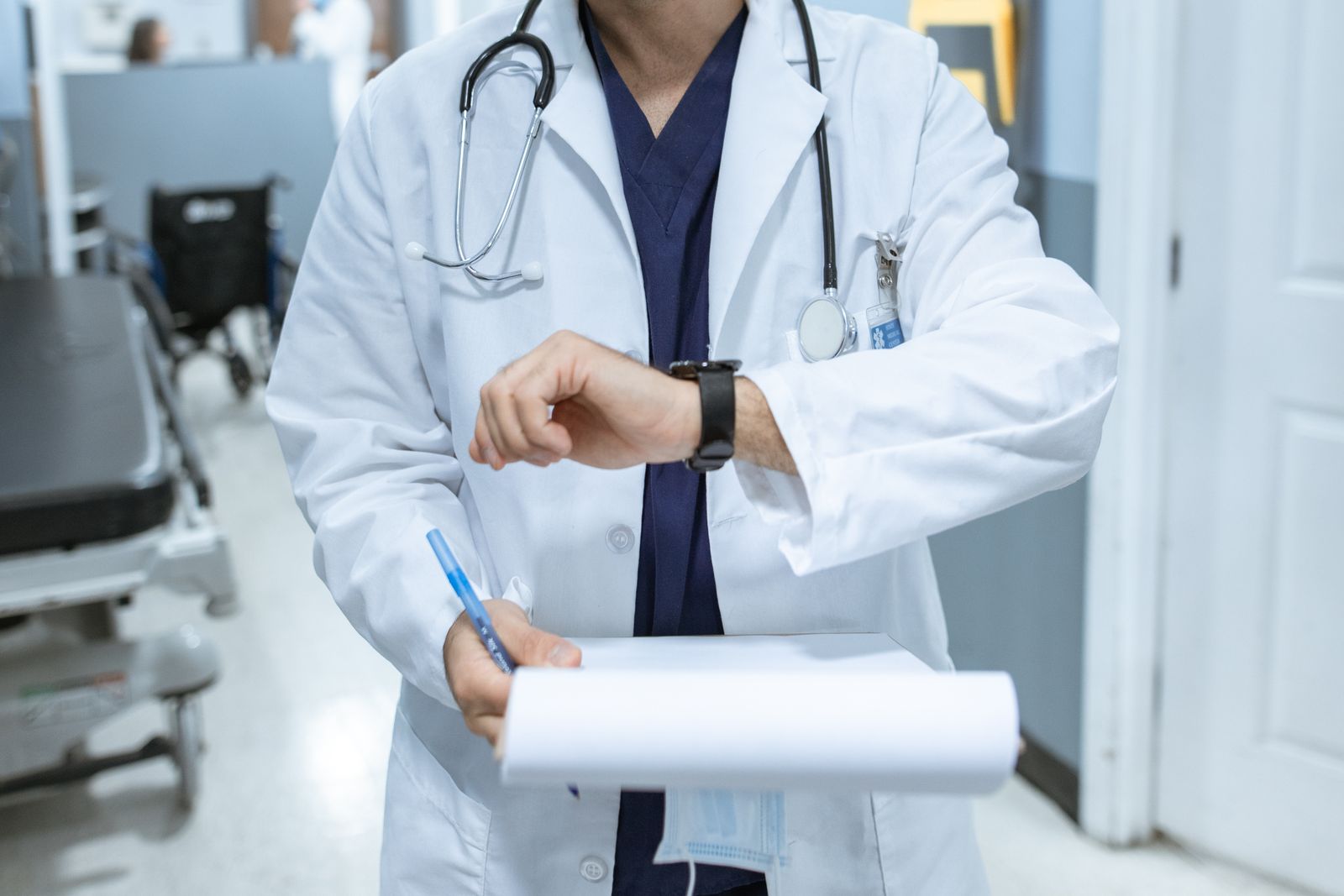 Ärztin im weißen Kittel geht mit einer Patientenakte durch einen Klinikflur und schaut auf ihre Armbanduhr – Patientenunterlagen gehören zu den Daten, die die Schweigepflicht im Auslandspraktikum schützt