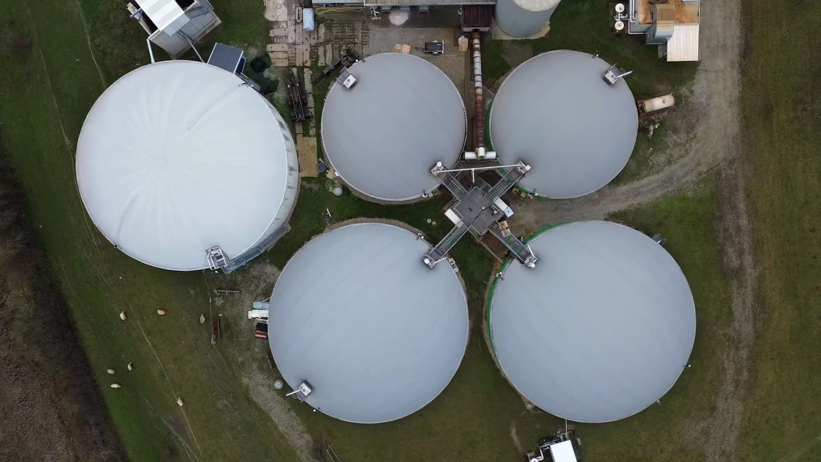 Aerial view of five large domed tanks in a green field, the kind of closed digester used to make biogas
