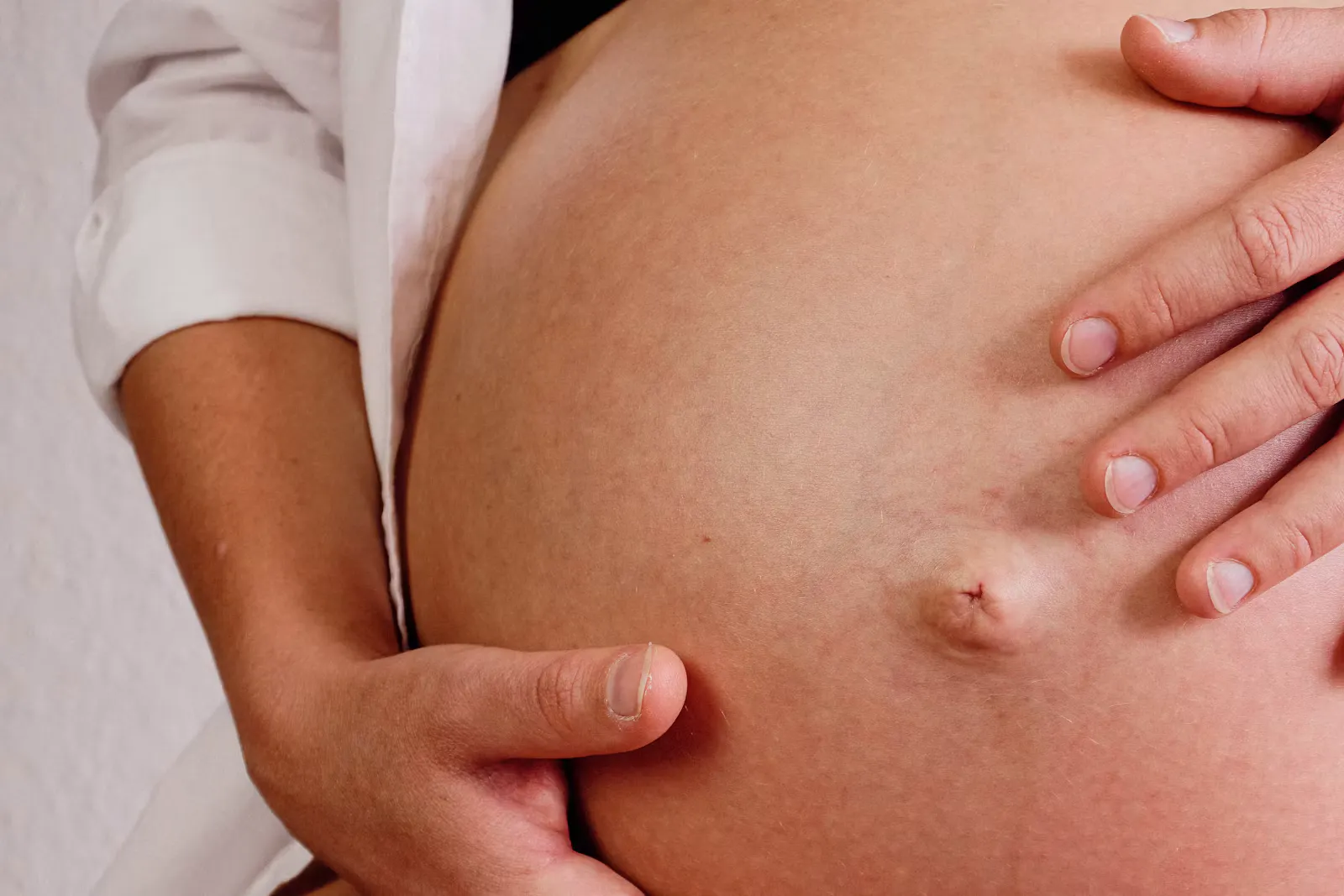 Nahaufnahme eines Babybauchs, zwei Hände liegen schützend darauf, Symbolbild für Schwangerschaft und Mutterschutz in Famulatur und PJ
