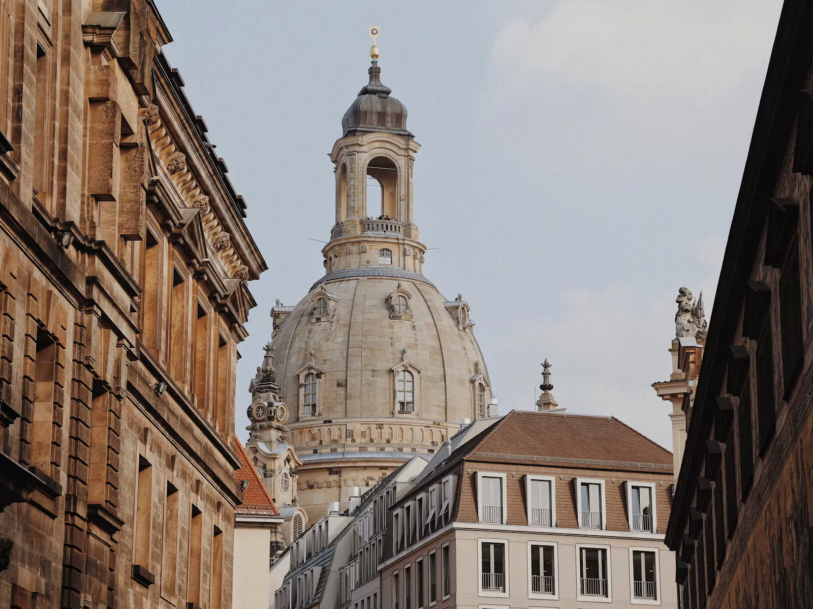 Kuppel der Dresdner Frauenkirche zwischen historischen Fassaden aus Sandstein unter hellem Himmel