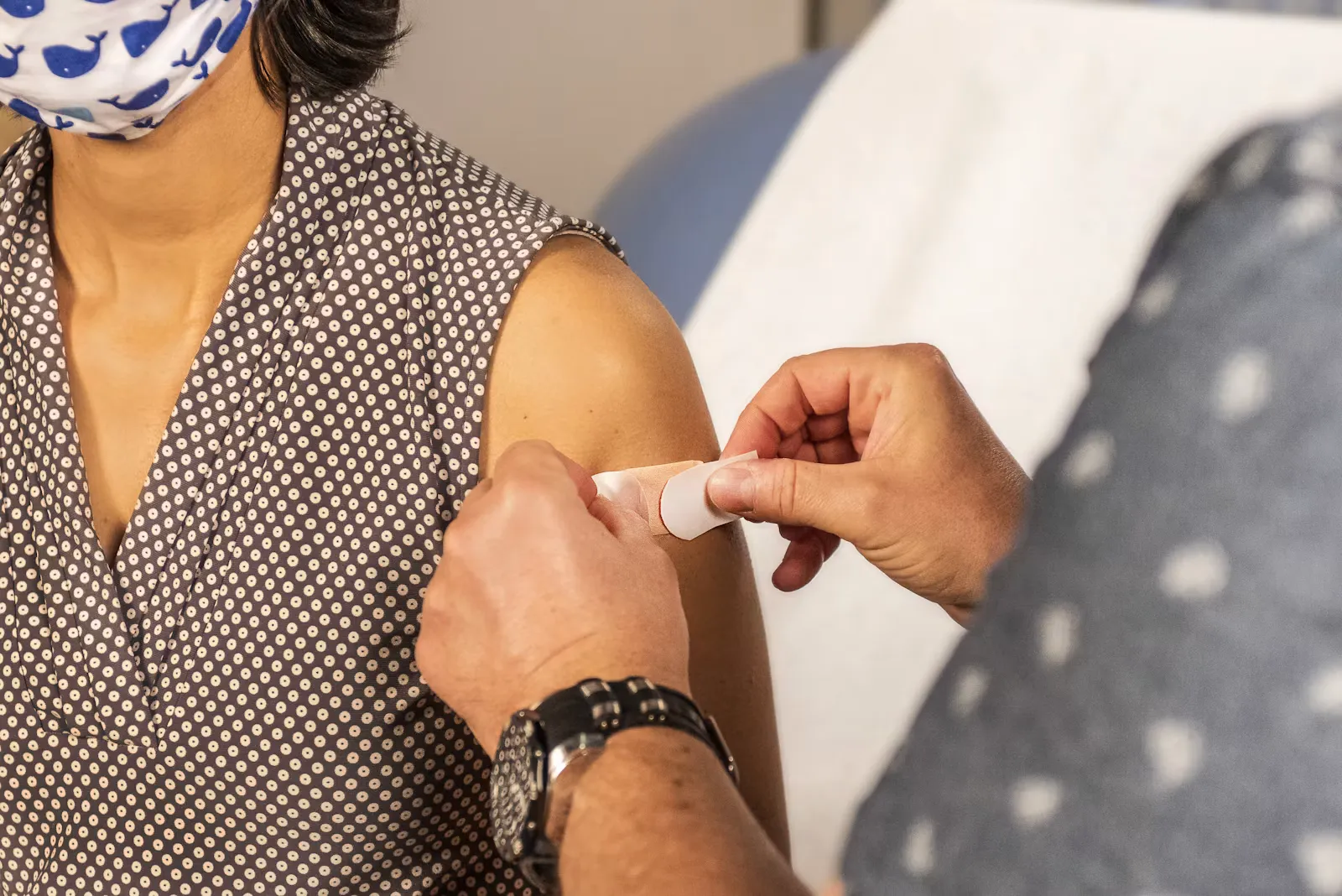 A clinician pressing a small plaster onto a patient's upper arm after an injection