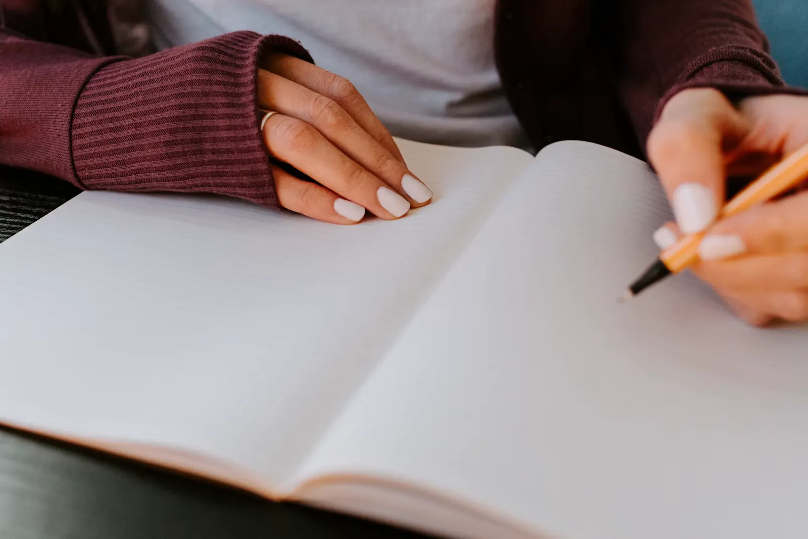 Two hands resting on an open ruled notebook, one holding a pencil ready to start writing